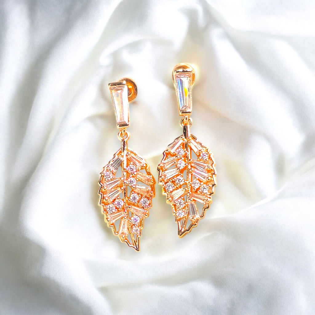 Elegant gold-plated leaf-shaped earrings with sparkling cubic zirconia stones, set against a luxurious white satin background