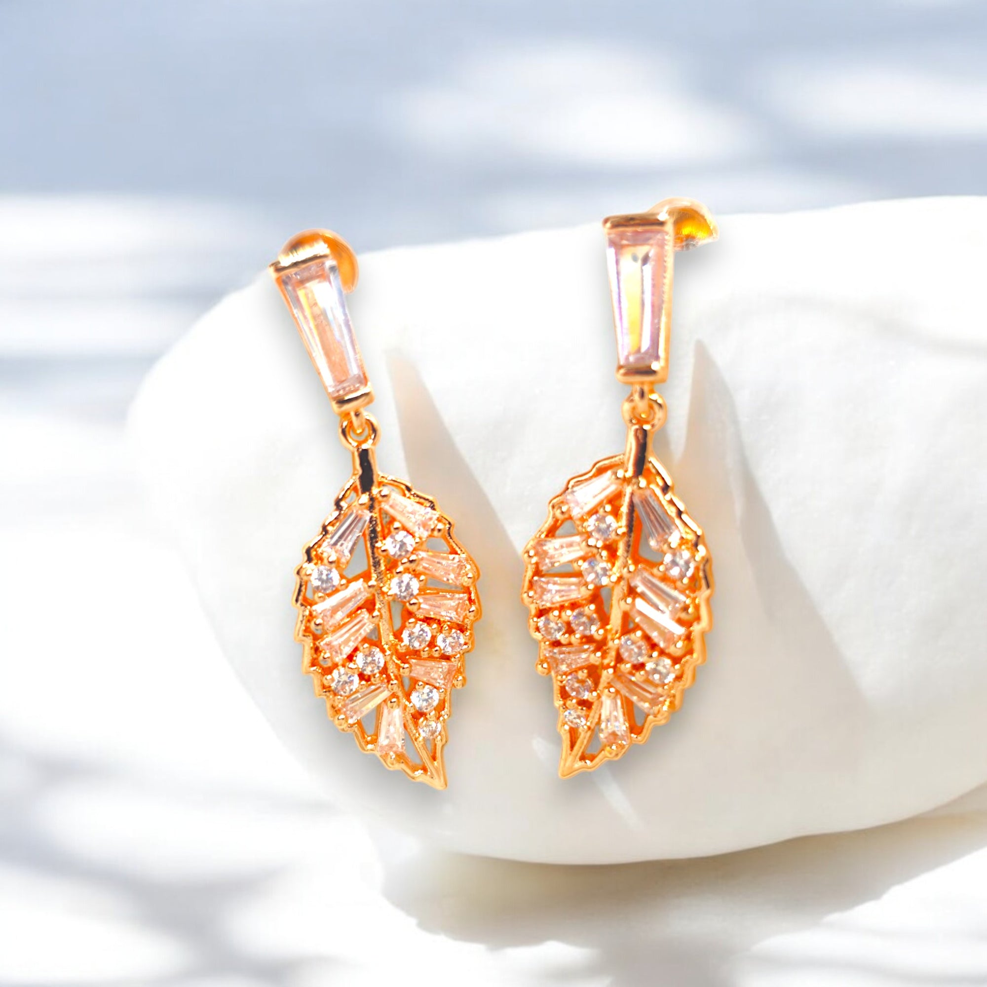 Elegant gold-plated leaf-shaped earrings with sparkling cubic zirconia stones, set against a luxurious white satin background