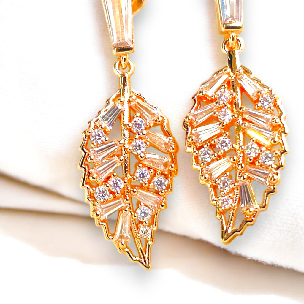 Elegant gold-plated leaf-shaped earrings with sparkling cubic zirconia stones, set against a luxurious white satin background