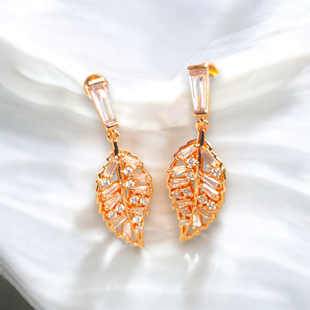 Elegant gold-plated leaf-shaped earrings with sparkling cubic zirconia stones, set against a luxurious white satin background