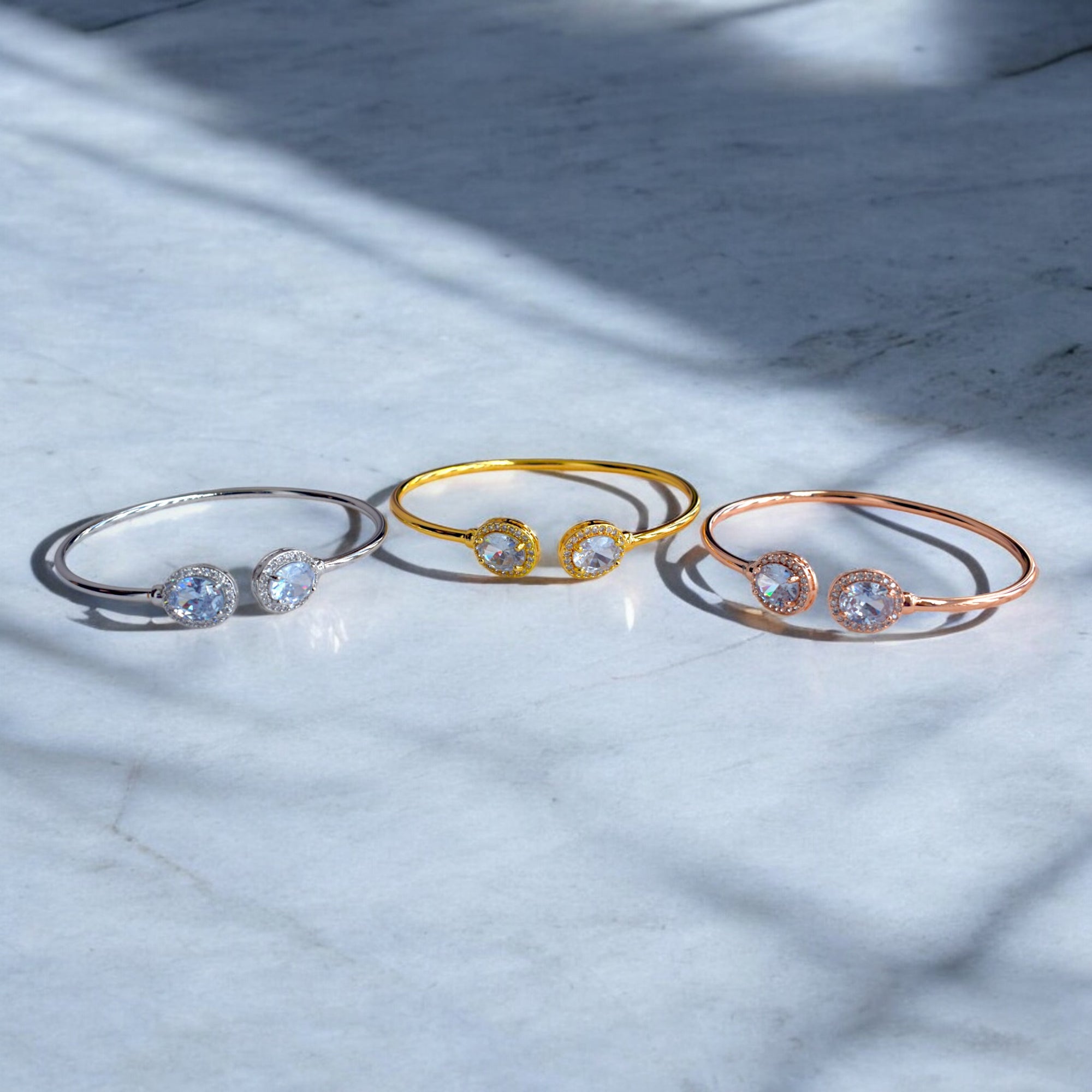 three diamond studded bangles in different colors rose gold silver and gold placed on a white marble floor