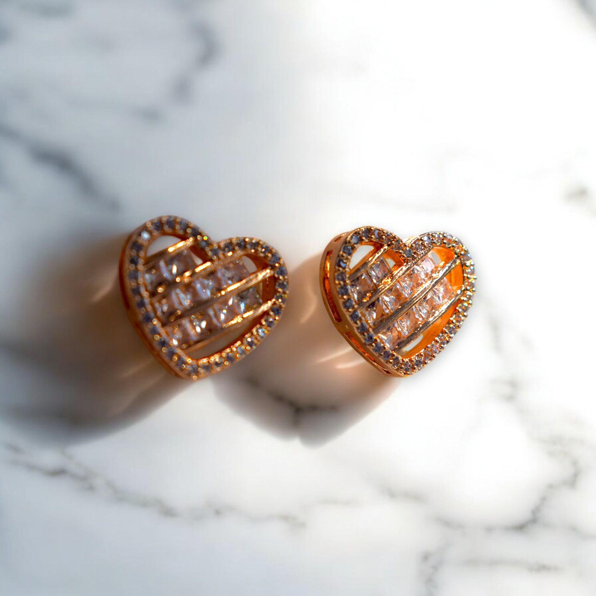 heart shaped zirconia stoned gold earrings placed on a white marble floor