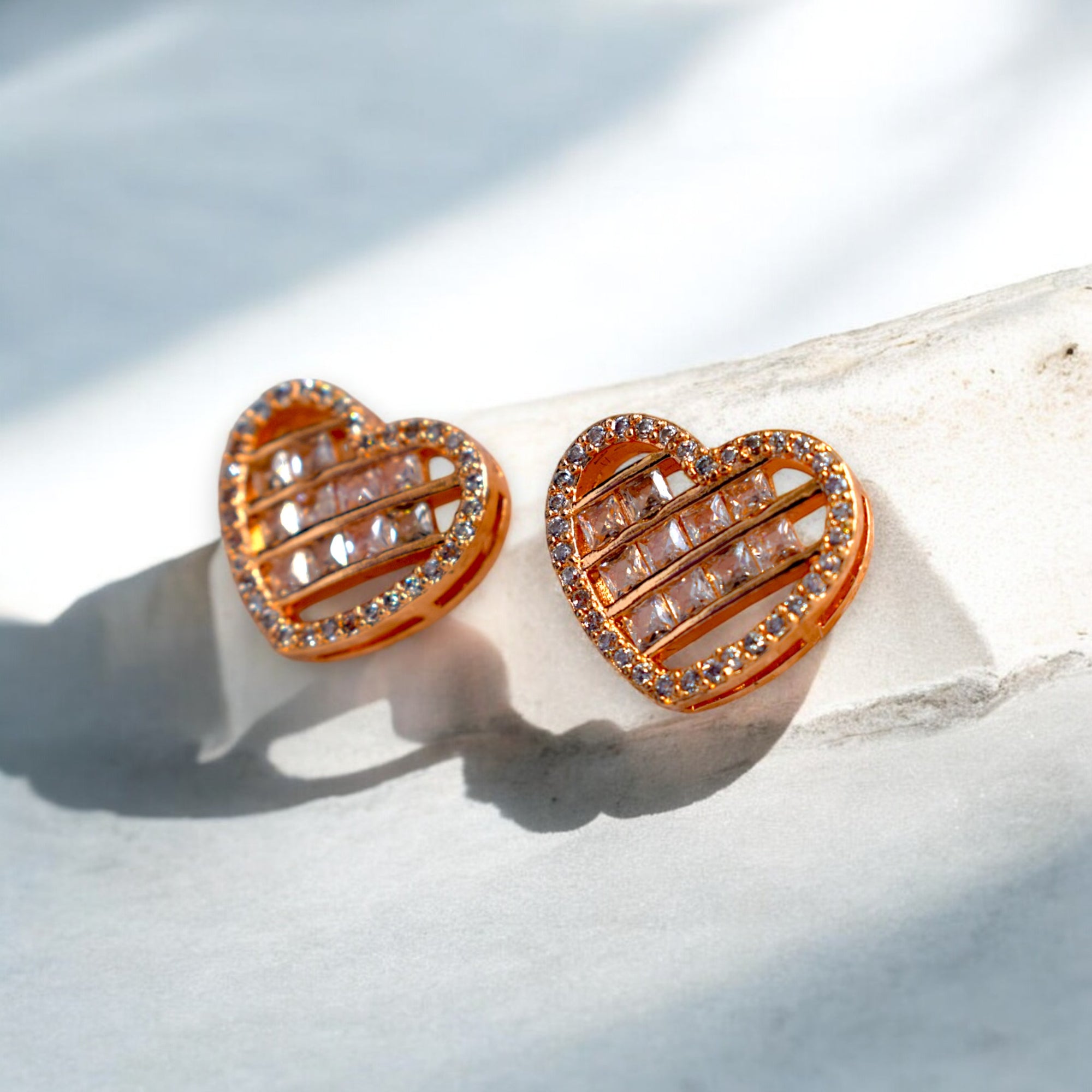 heart shaped zirconia stoned gold earrings placed on a white marble floor