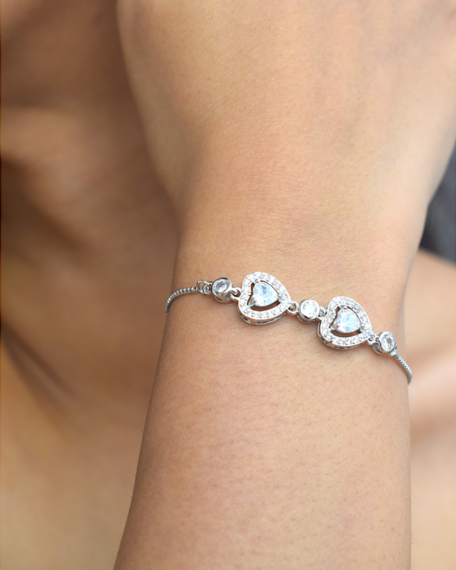 close up of a silver heart shaped diamond chain bracelet worn by a girl
