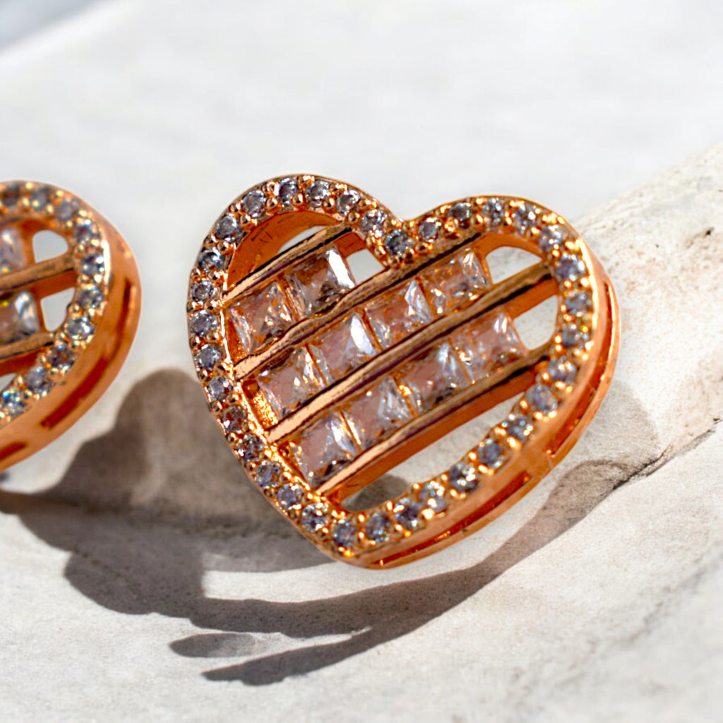 close up of a heart shaped zirconia stoned gold earrings placed on a white marble floor