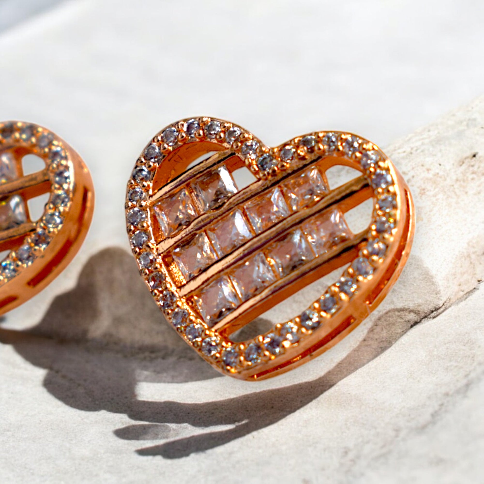 close up of a heart shaped zirconia stoned gold earrings placed on a white marble floor