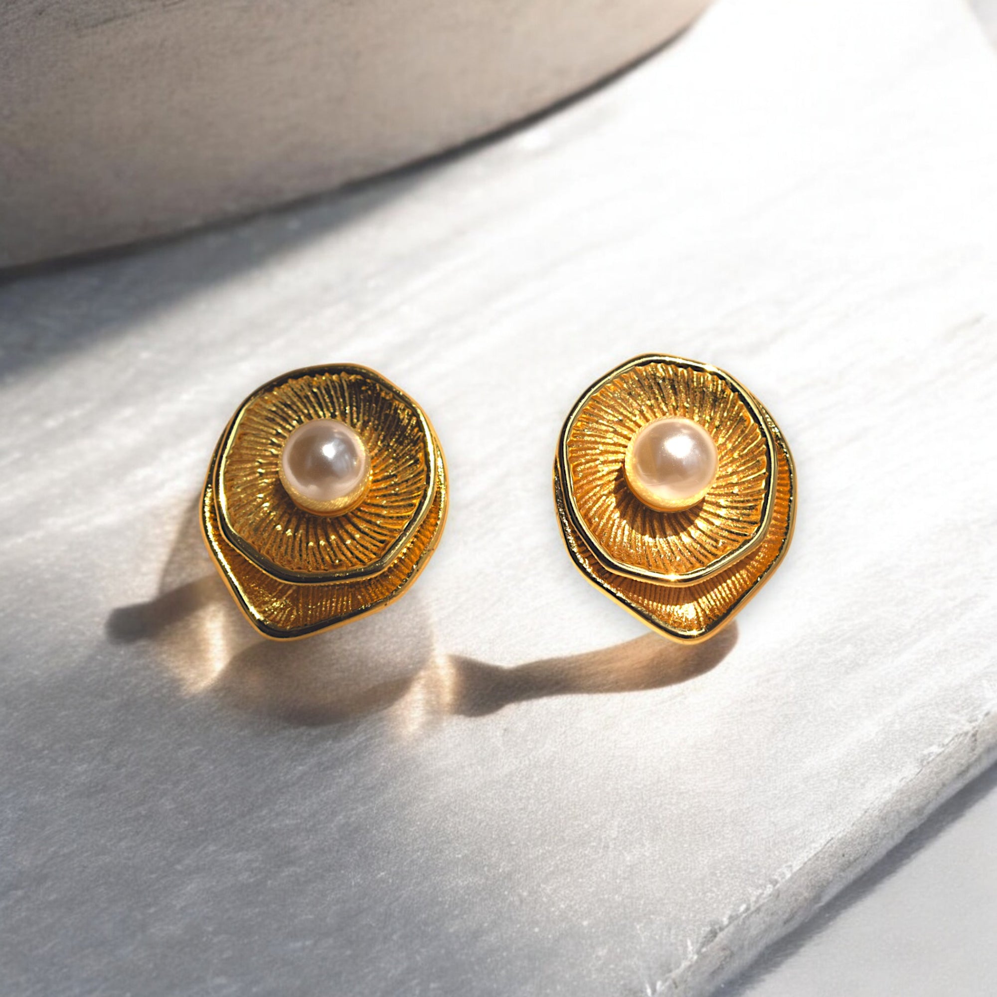 Golden round earring with a pearl at the center placed on a white marble floor