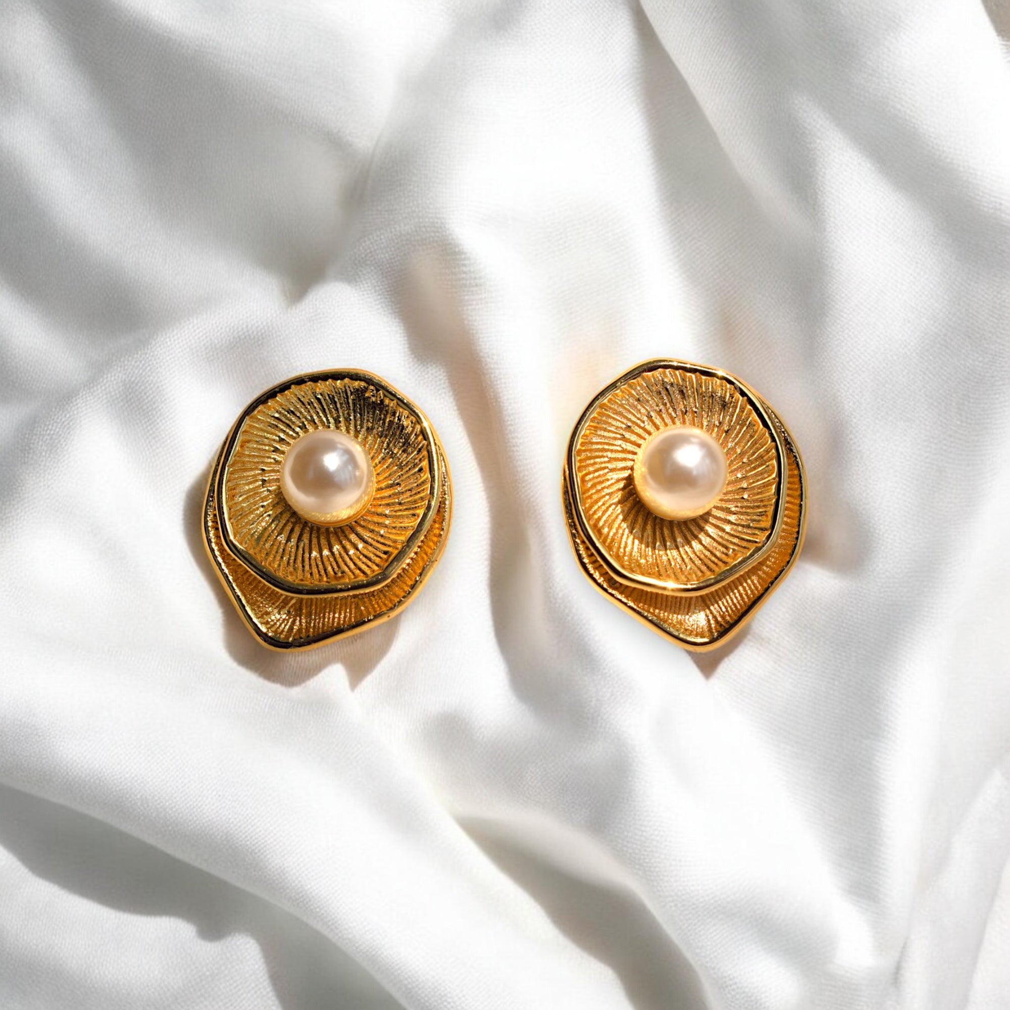 Golden round earring with a pearl at the center placed on a white satin cloth 