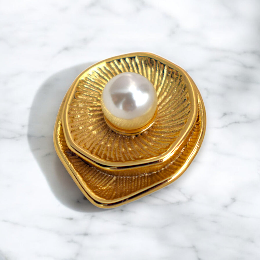A single golden round earring with a pearl at the center placed on a white marble floor