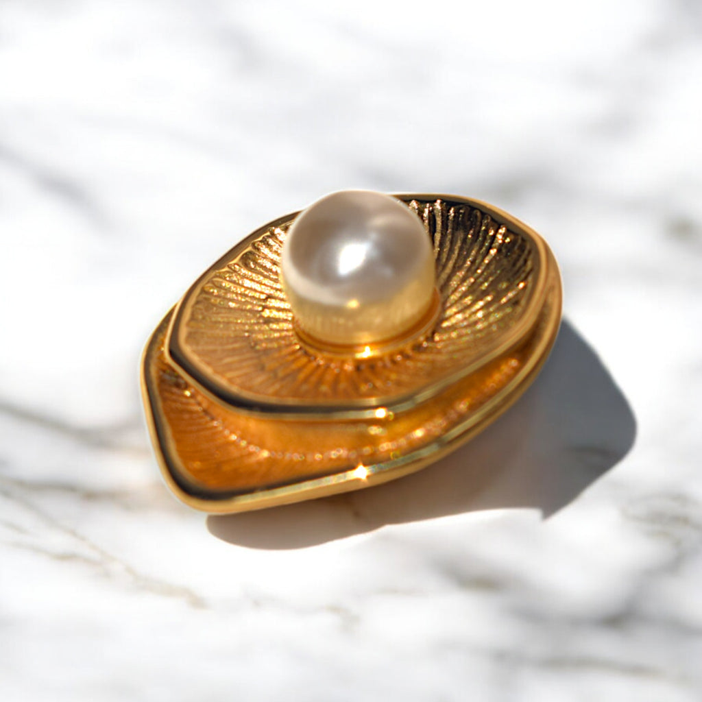 Side view of a single golden round earring with a pearl at the center placed on a white marble floor