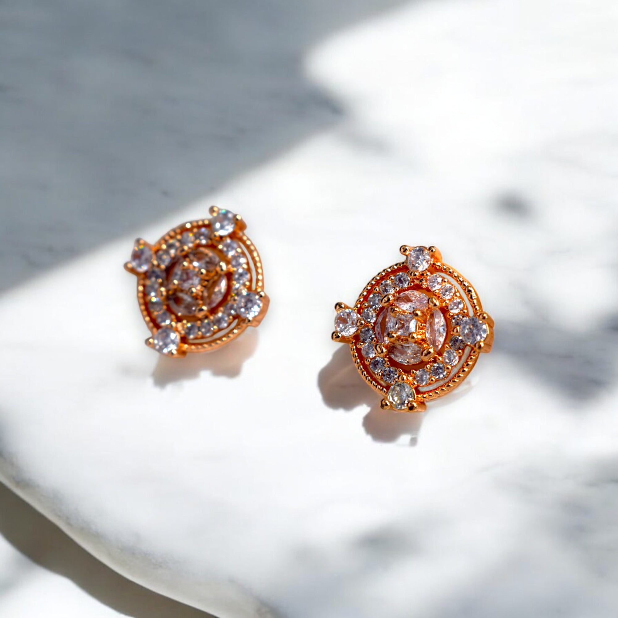 Round Gold zirconia stoned earrings placed on a white marble floor