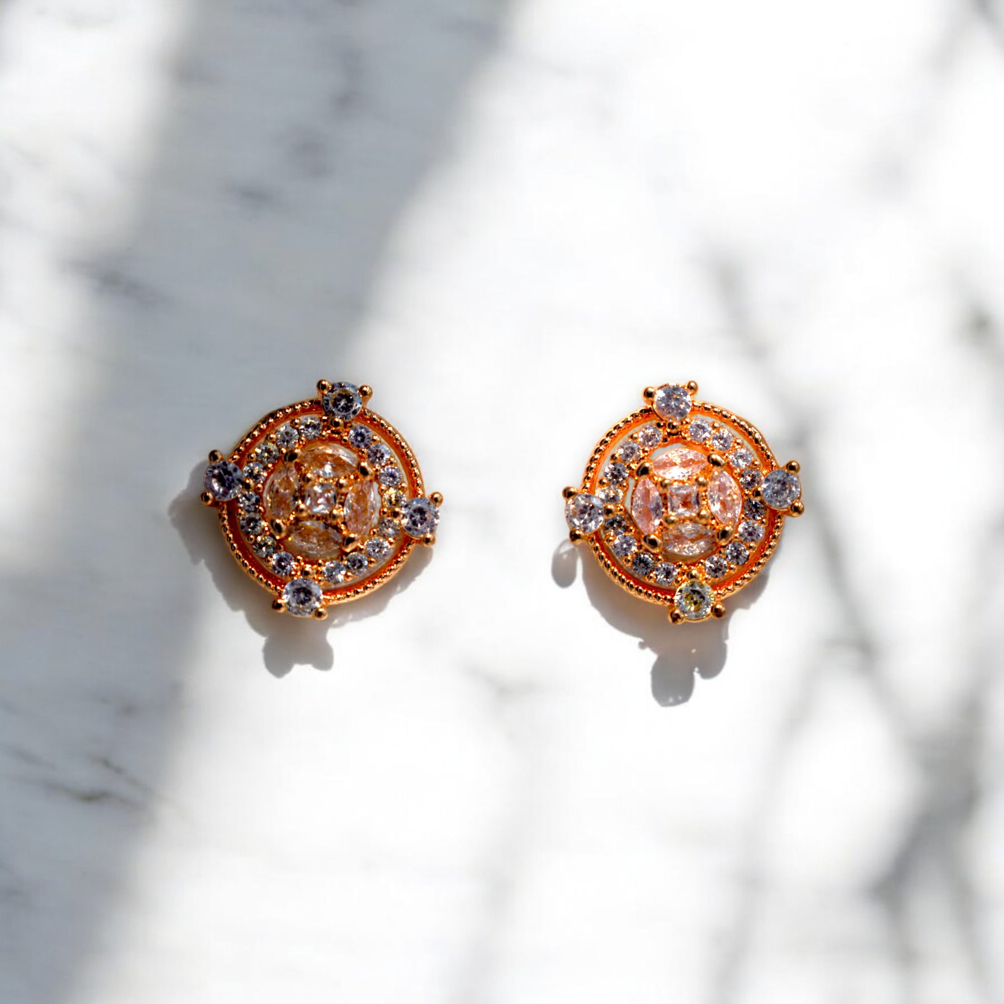 Round Gold zirconia stoned earrings placed on a white marble floor