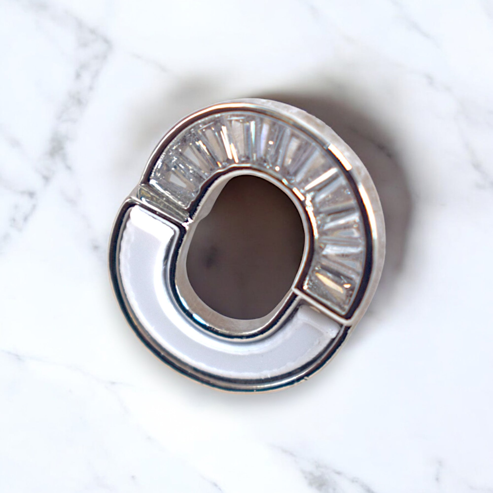 close up of kansobi single silver round zirconia stone earrings on a white marble floor