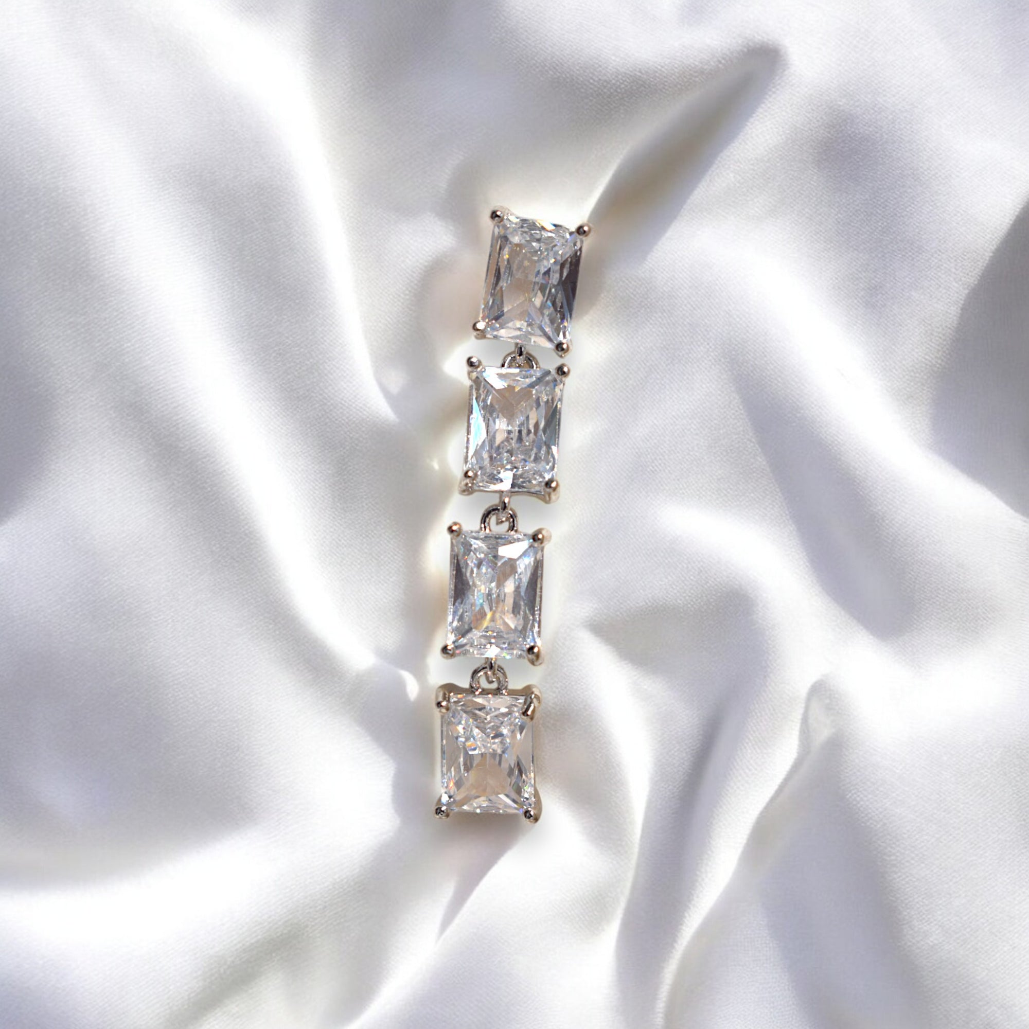 A single earring which is a silver zirconia stoned earring on a white satin cloth