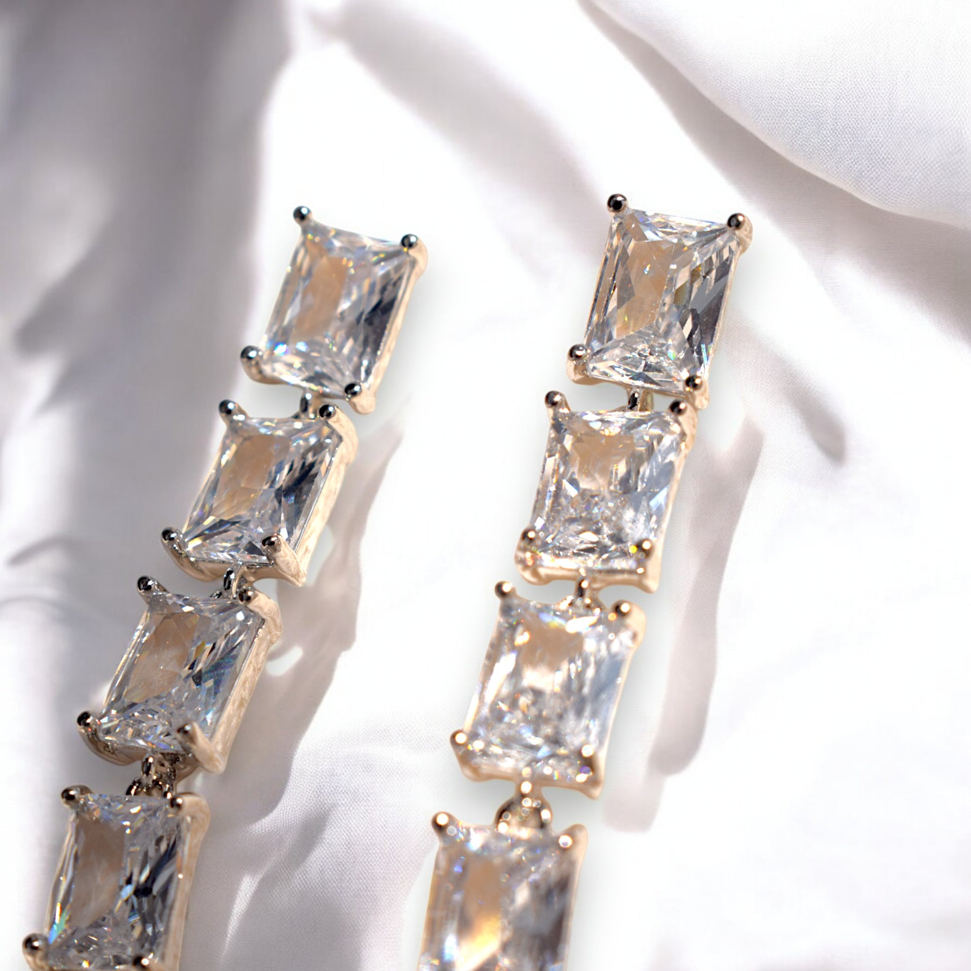 Close up of a silver zirconia stoned diamond earring on a white satin cloth background