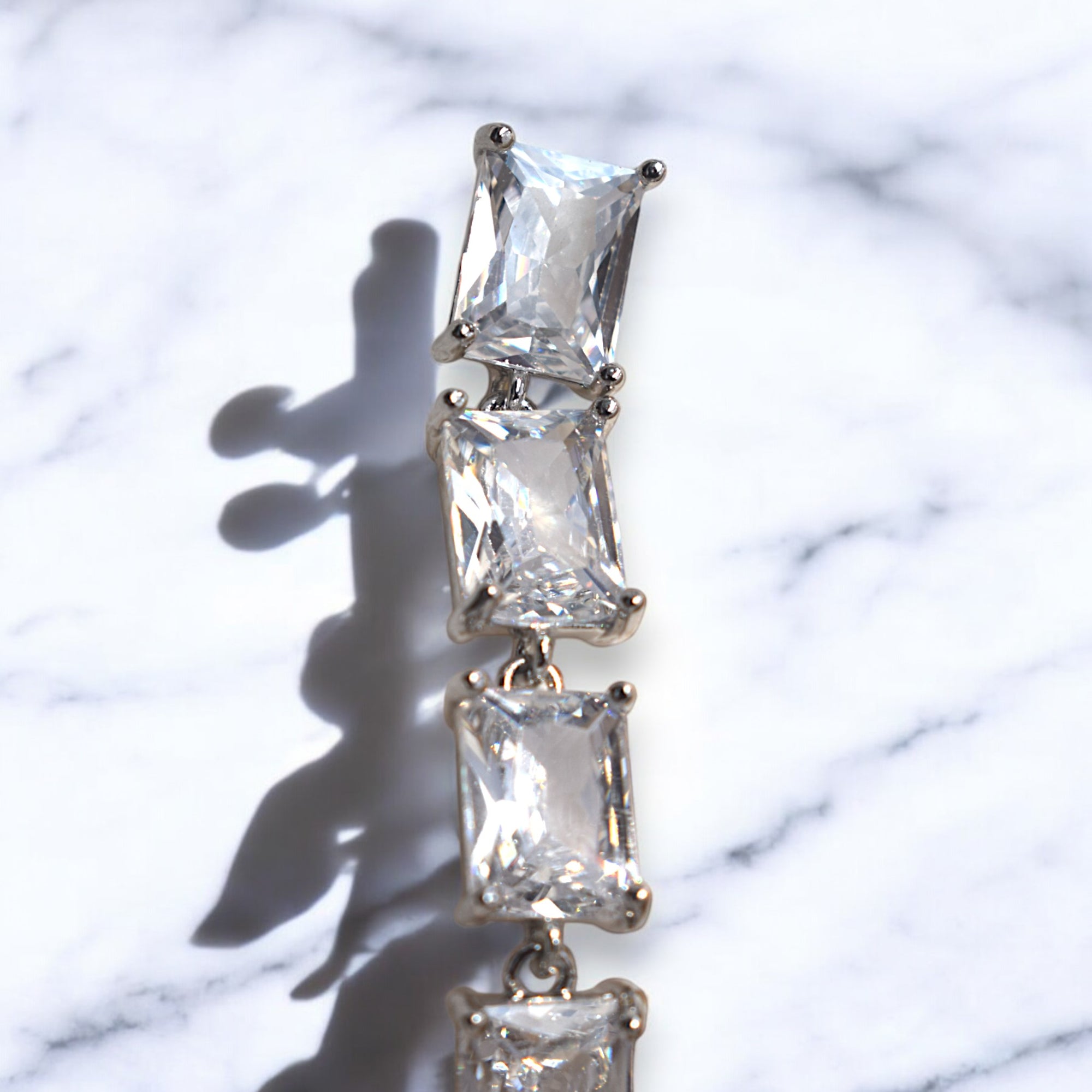 Close up of a silver zirconia stoned diamond earring on a white marble floor