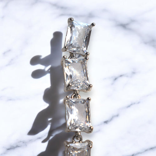 Close up of a silver zirconia stoned diamond earring on a white marble floor