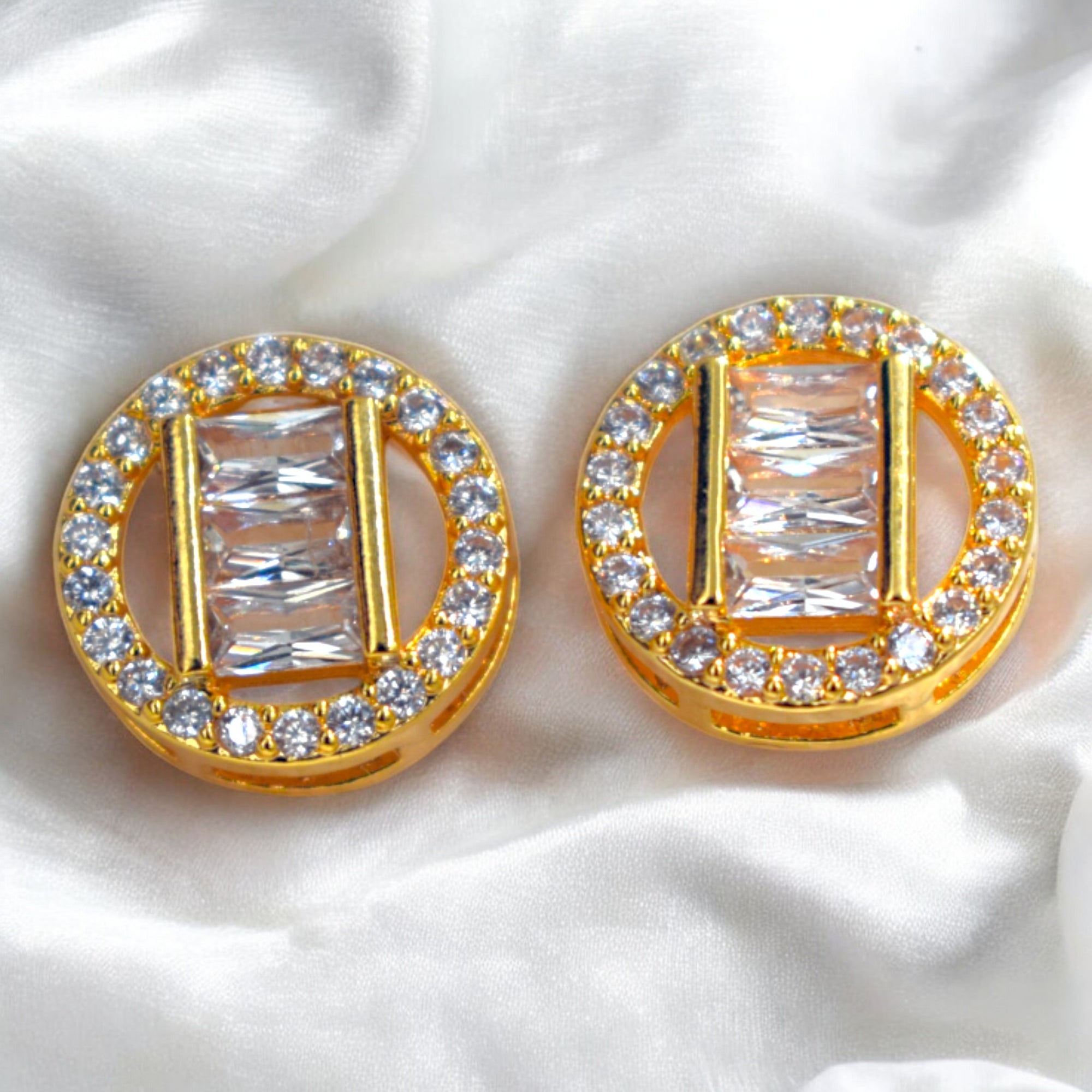 Gold earrings with rectangular gemstones on a white fabric background