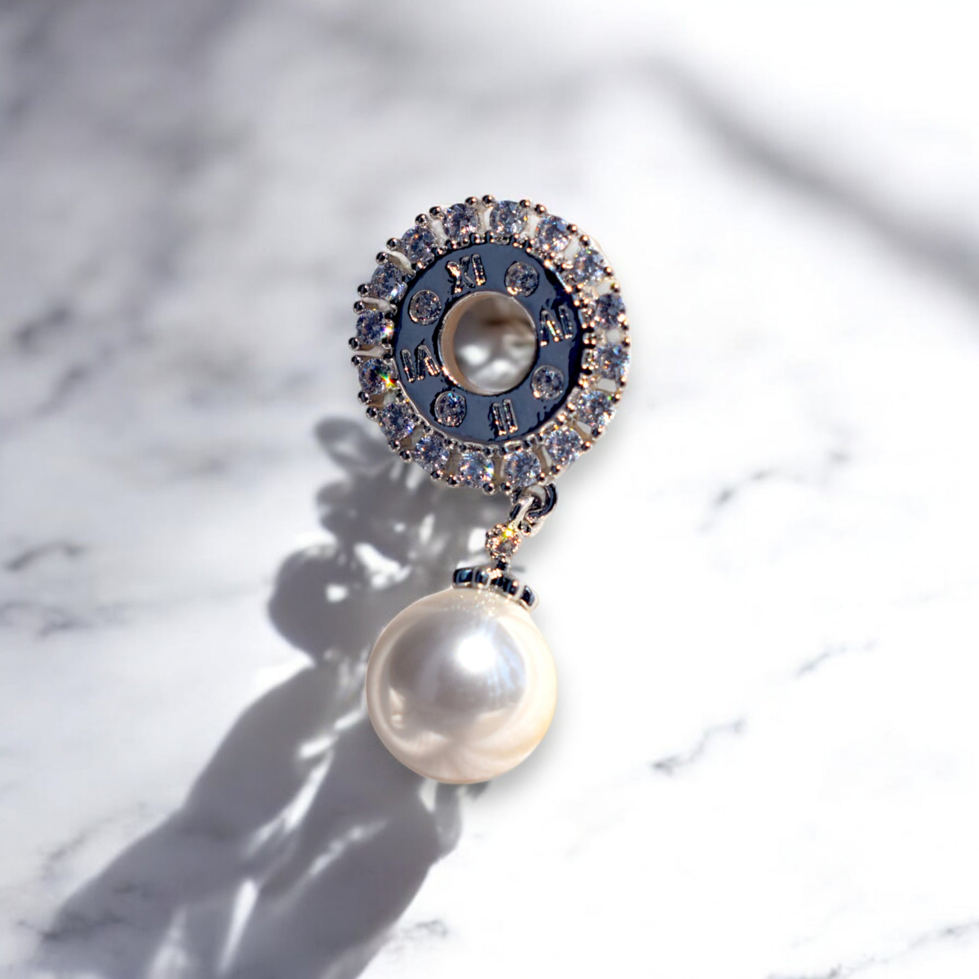 A single zirconia stone studded silver pearl drop earring on a white marble countertop