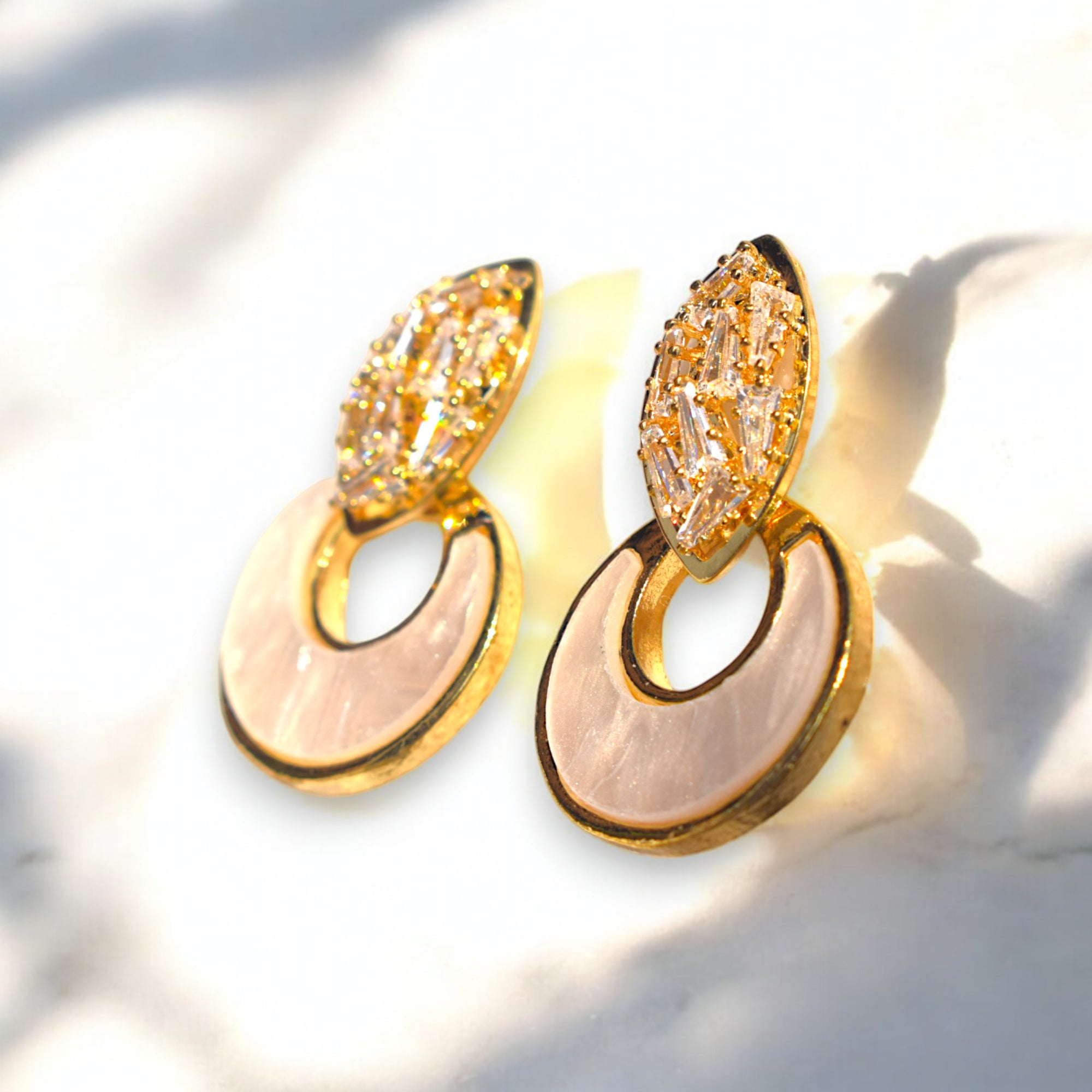 side view of two golden crescent moon zirconia stone studded earrings on a white marble floor