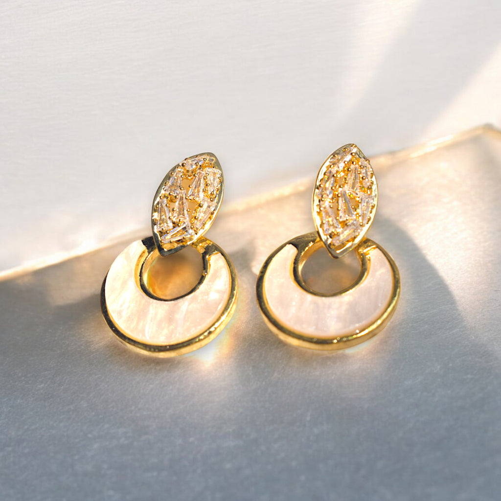 two golden crescent moon zirconia stone studded earrings on a marble floor