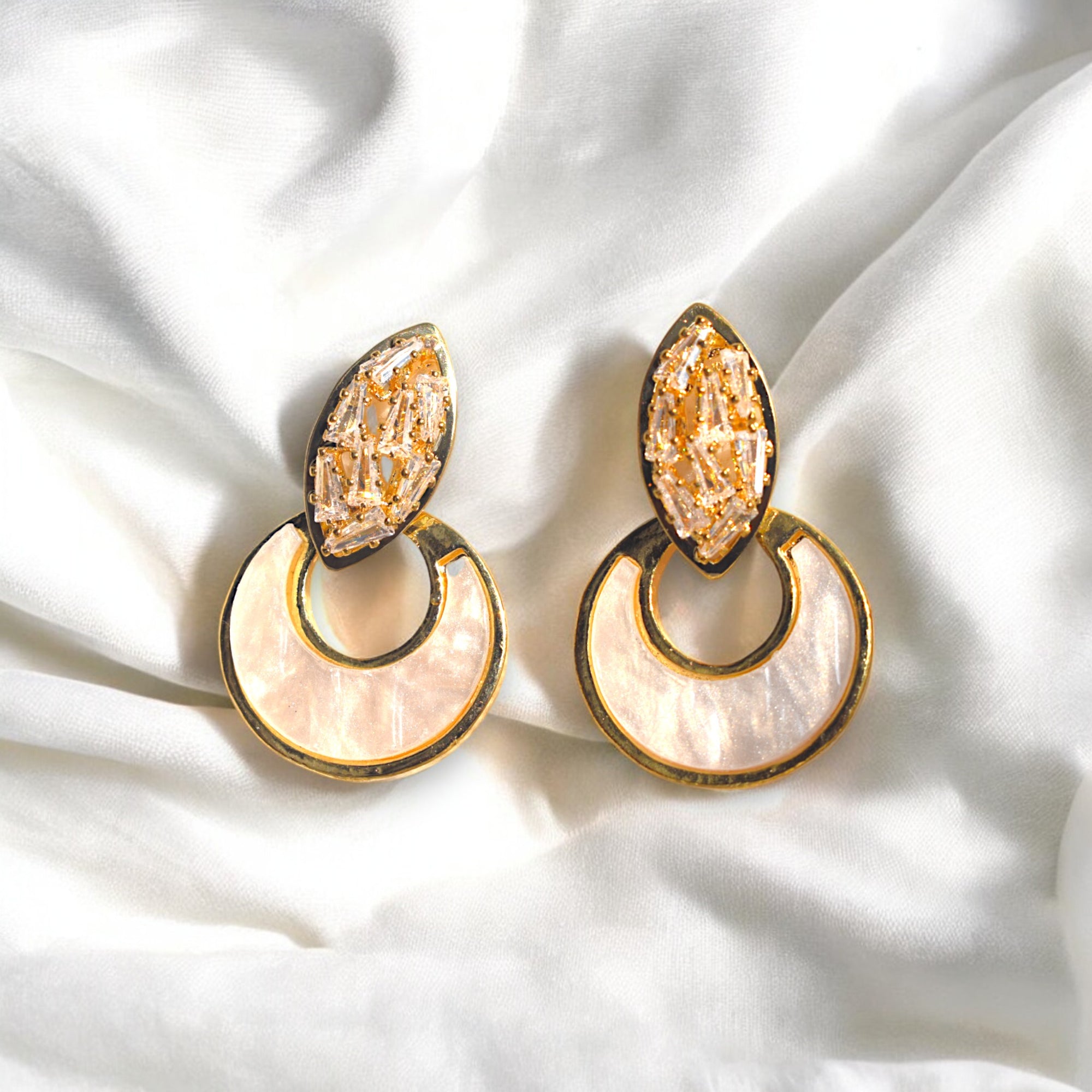 two golden crescent moon zirconia stone studded earrings on a white satin cloth
