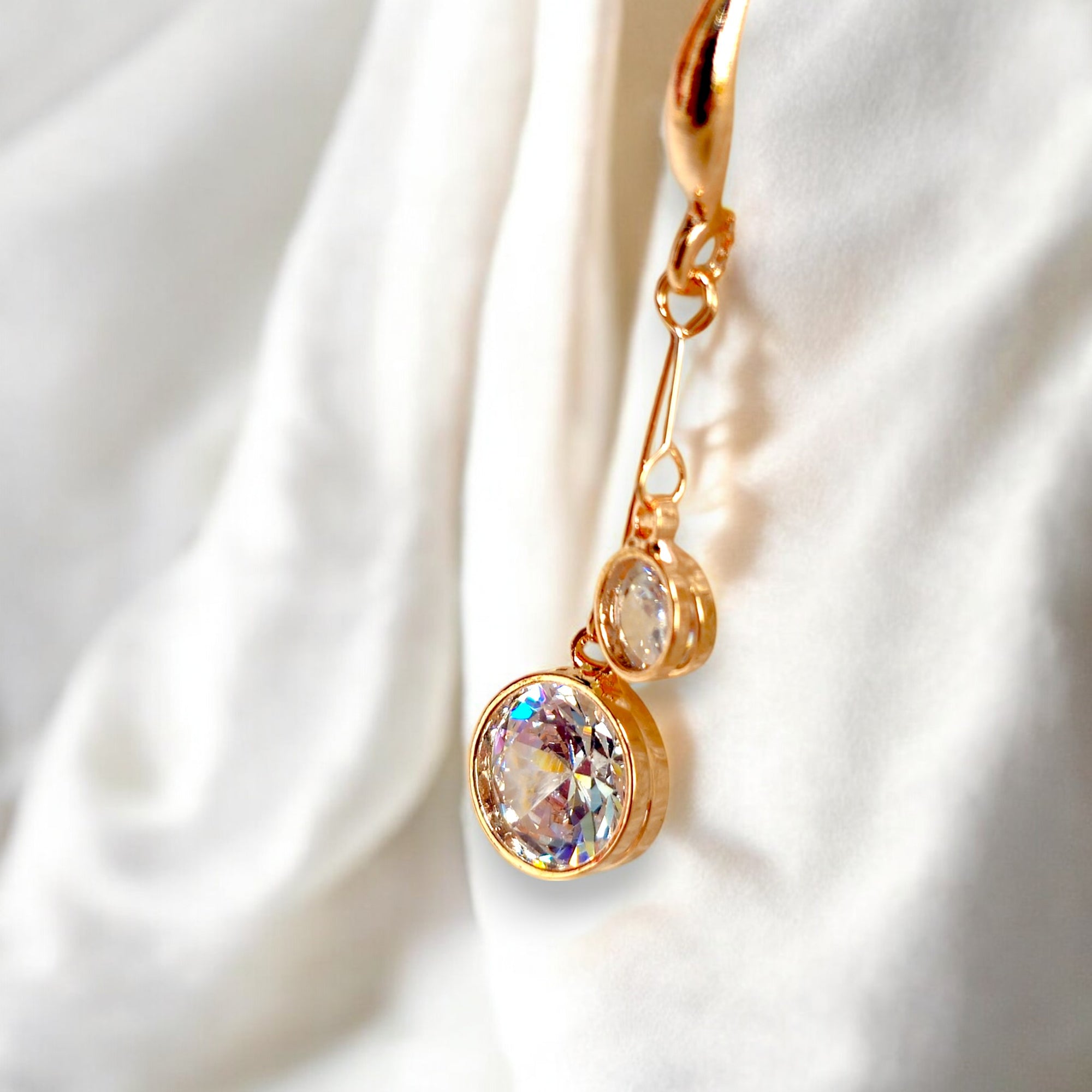 kansobi single rose gold drop earrings with round zirconia diamonds placed on a white satin cloth