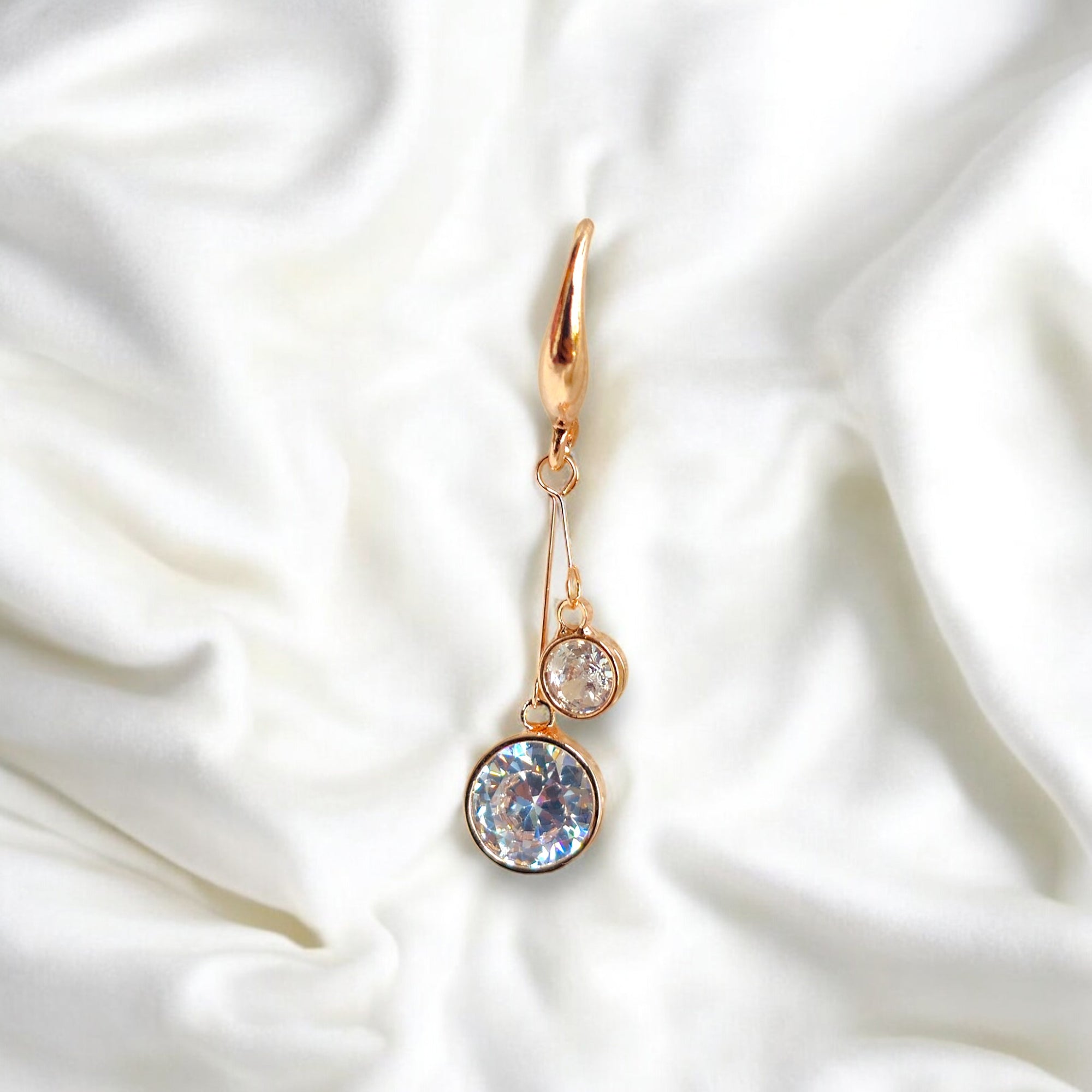 kansobi single rose gold drop earrings with round zirconia diamonds placed on a white satin cloth
