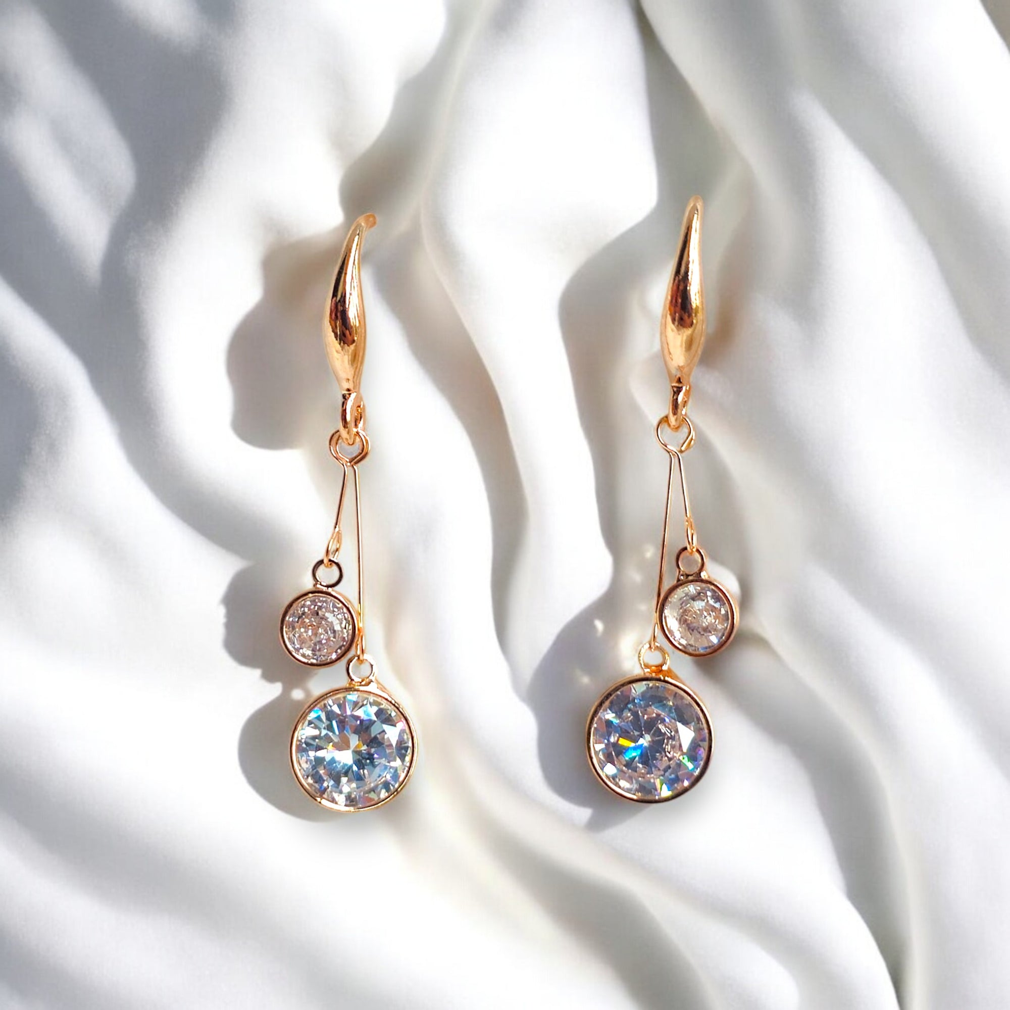 kansobi rose gold drop earrings with round zirconia diamonds placed on a white satin cloth