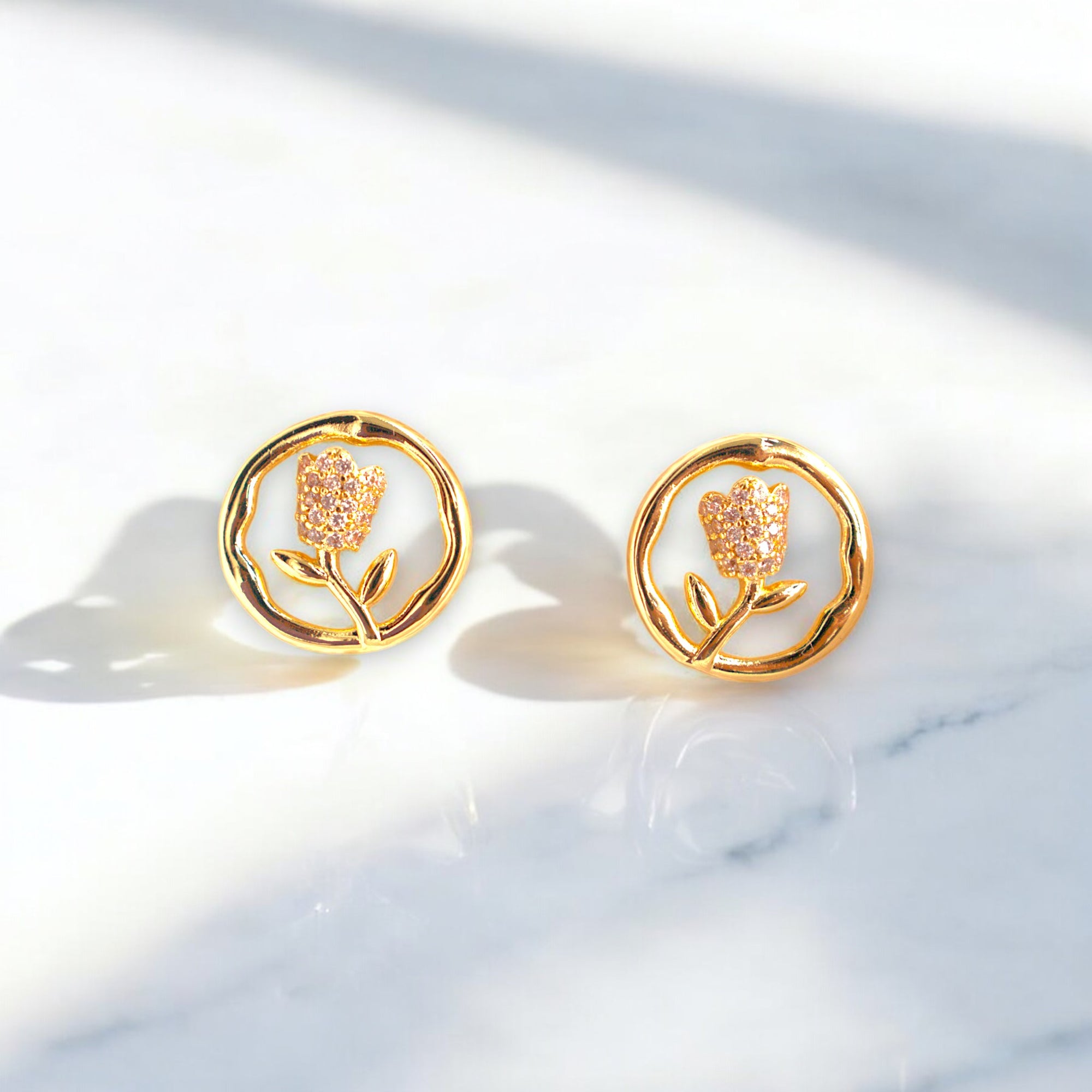 14K gold round flower earrings with Zirconia stones placed on a white marble floor