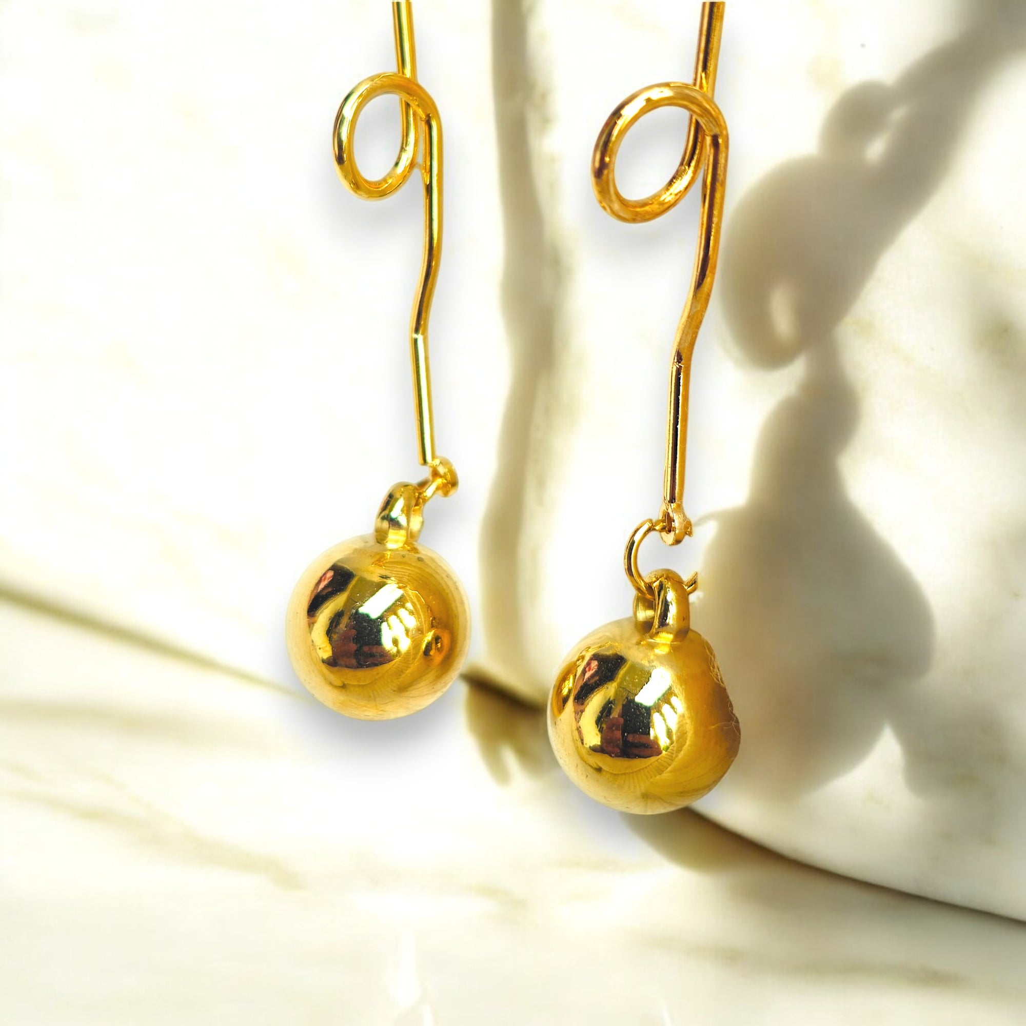 Gold plated dangle earrings with a minimalist orb design in a marble background