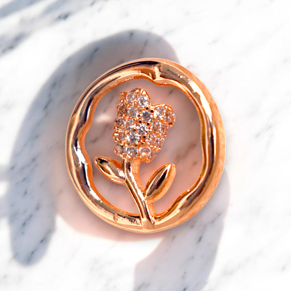 Single rose gold round flower earrings with Zirconia stones placed on a white marble countertop