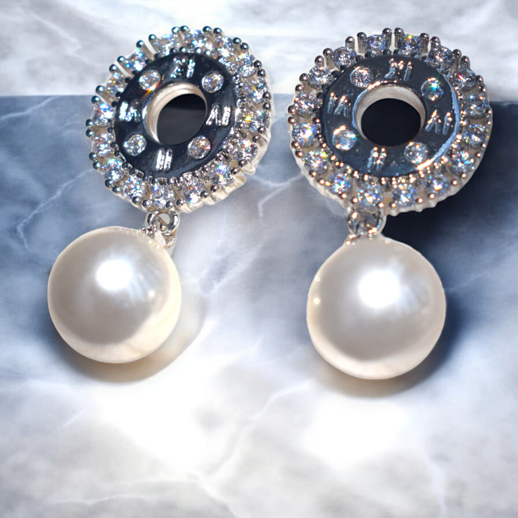 shining zirconia stone studded silver pearl drop earrings on a white marble floor