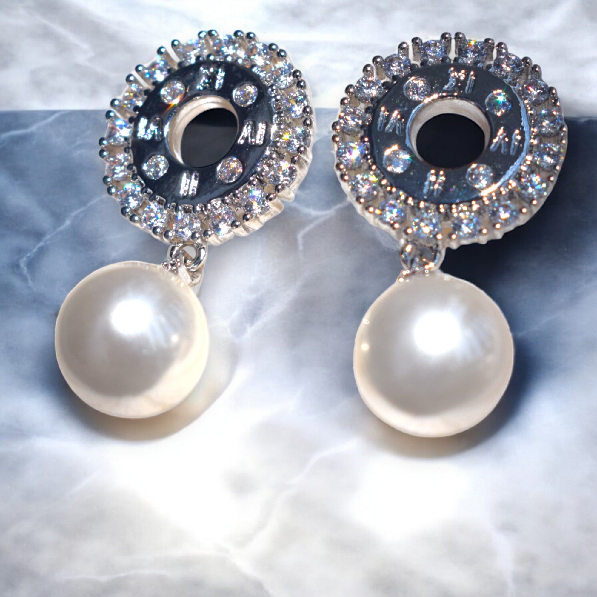 shining zirconia stone studded silver pearl drop earrings on a white marble floor