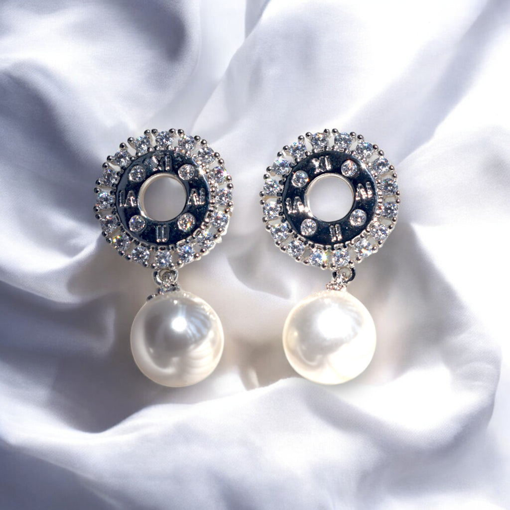 zirconia stone studded silver pearl drop earrings on a white satin cloth