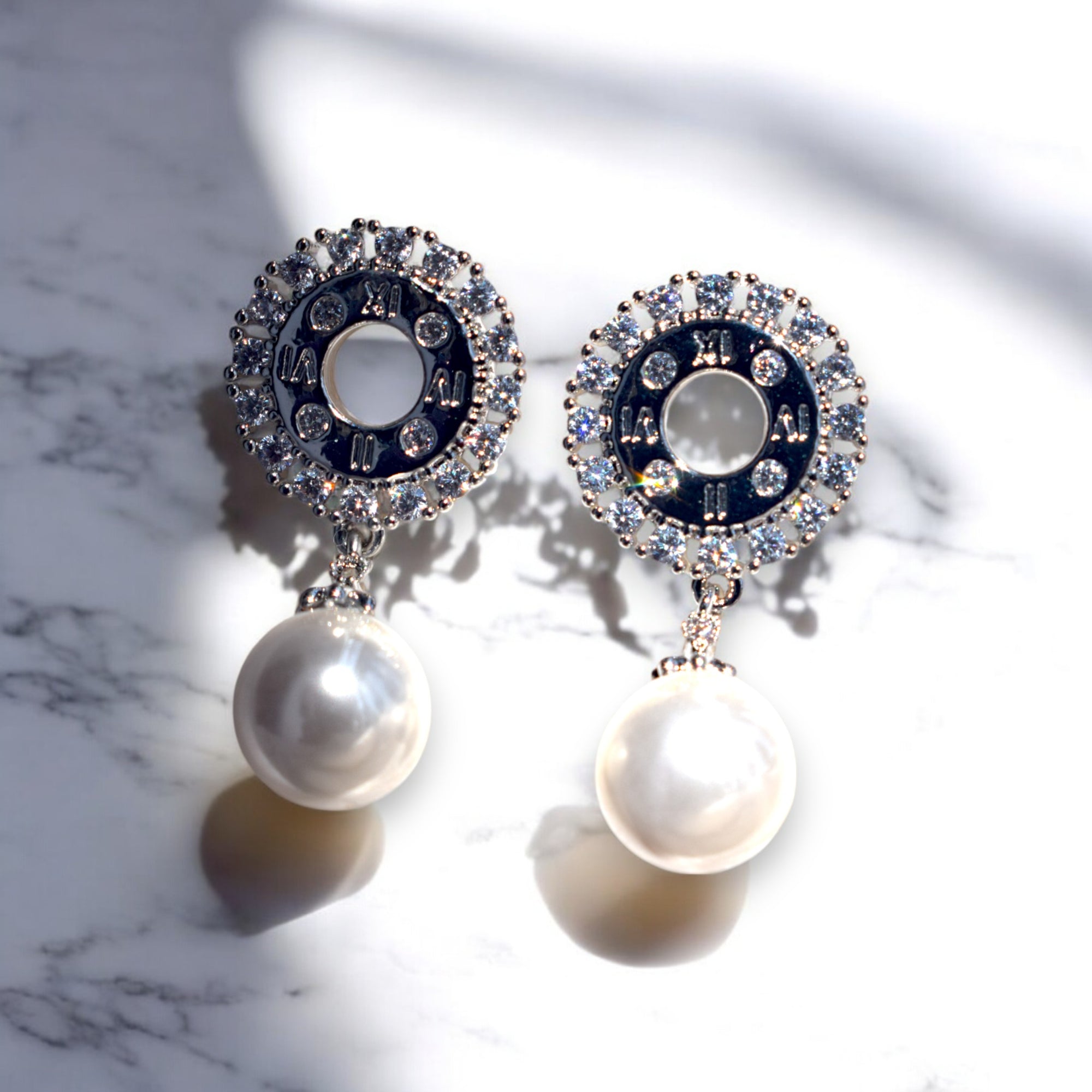 zirconia stone studded silver pearl drop earrings on a white marble floor kept under the sun