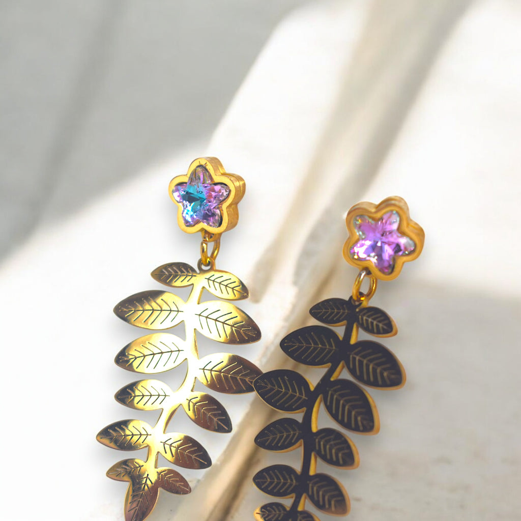 14k golden fern leaf earring with zirconia star diamonds on a white marble floor