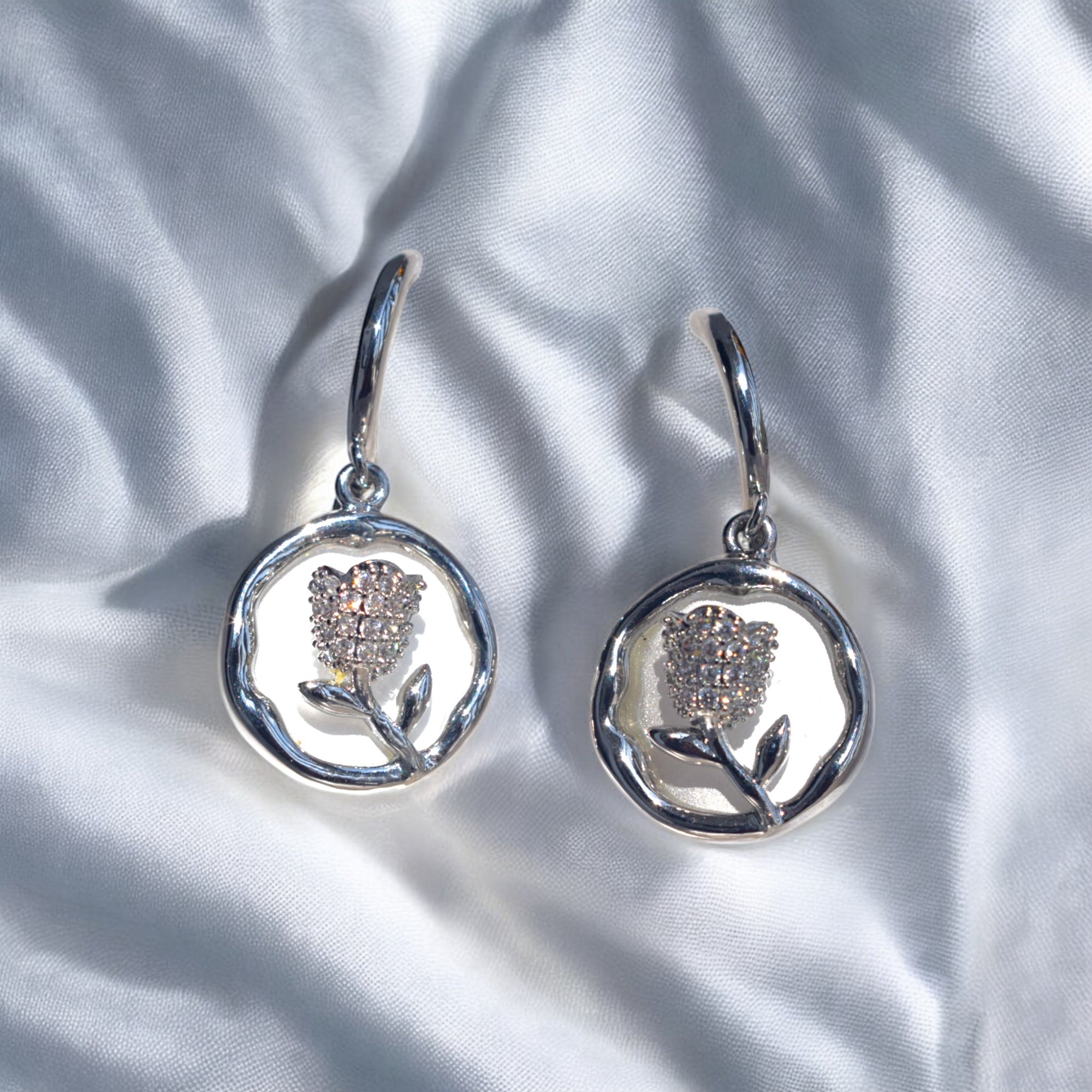 silver round flower earrings with Zirconia stones placed on a white satin cloth