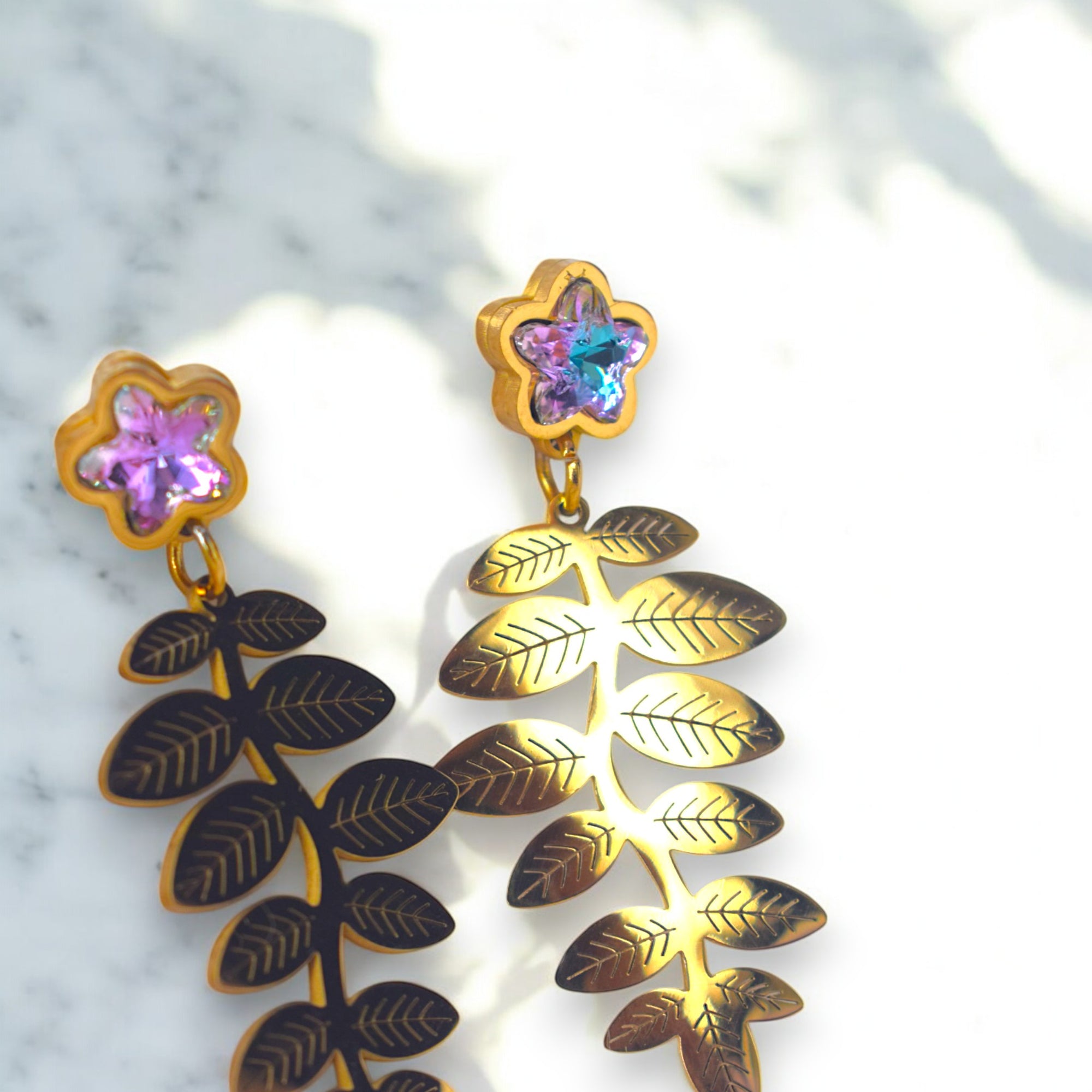 14k golden fern leaf earring with zirconia star diamonds on a white marble floor