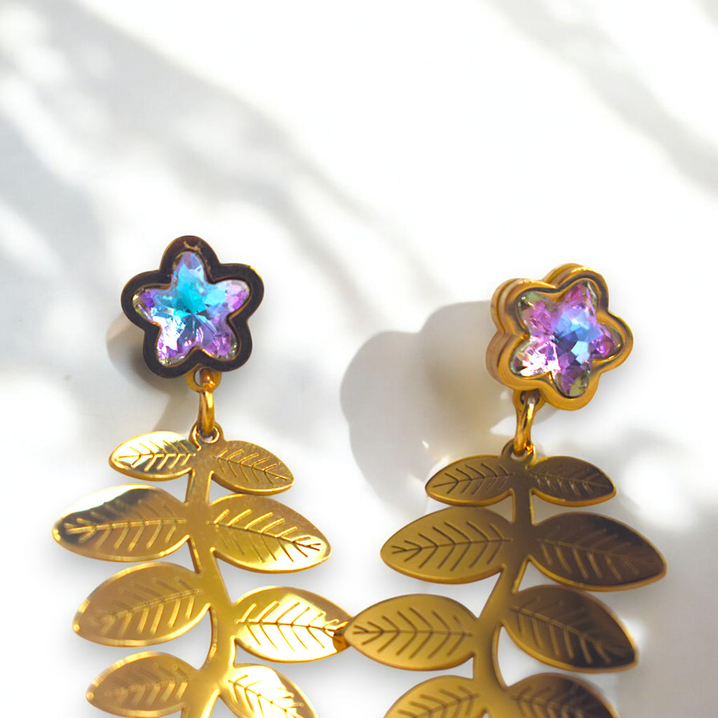 Close up of a 14k golden fern leaf earring with zirconia star diamonds on a white marble floor