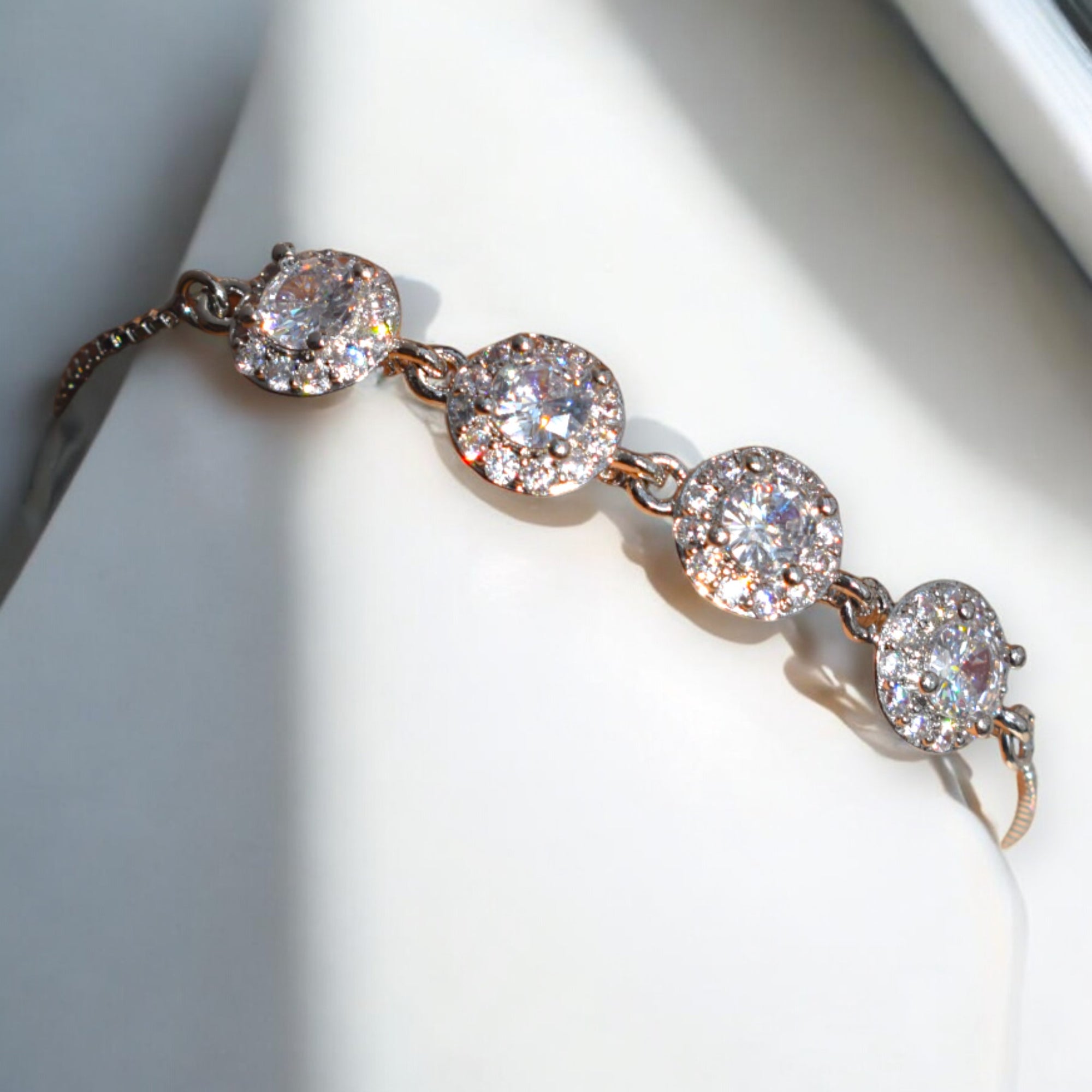 Diamond stoned silver circle chain bracelet on a white stand where the sun shines on it