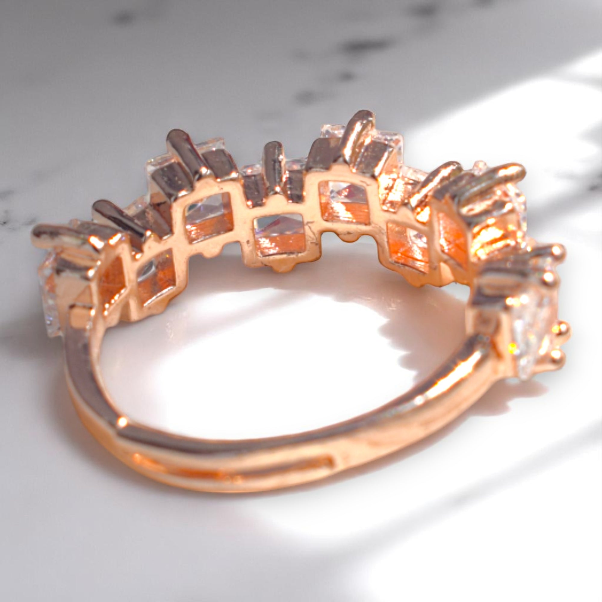 Rose gold ring with clear gemstones on a marble surface