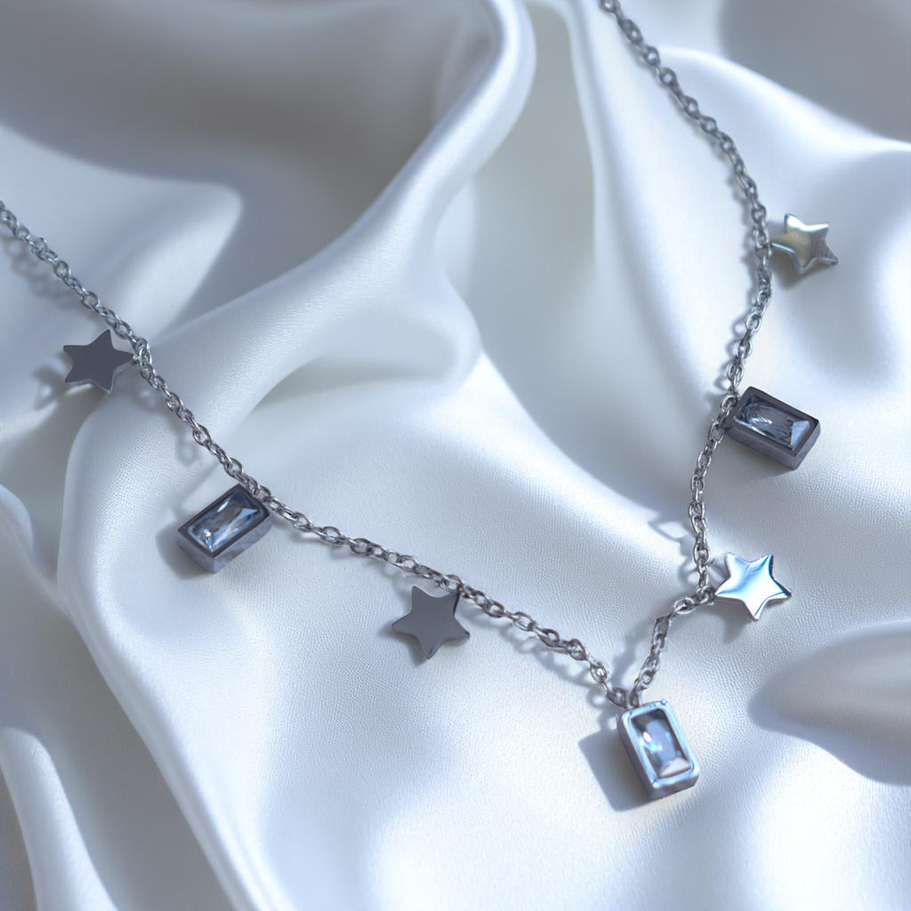Silver necklace with star and rectangular pendant on a white fabric background
