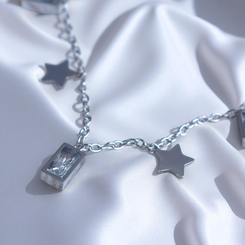 Silver bracelet with star and cube charms on a white fabric background
