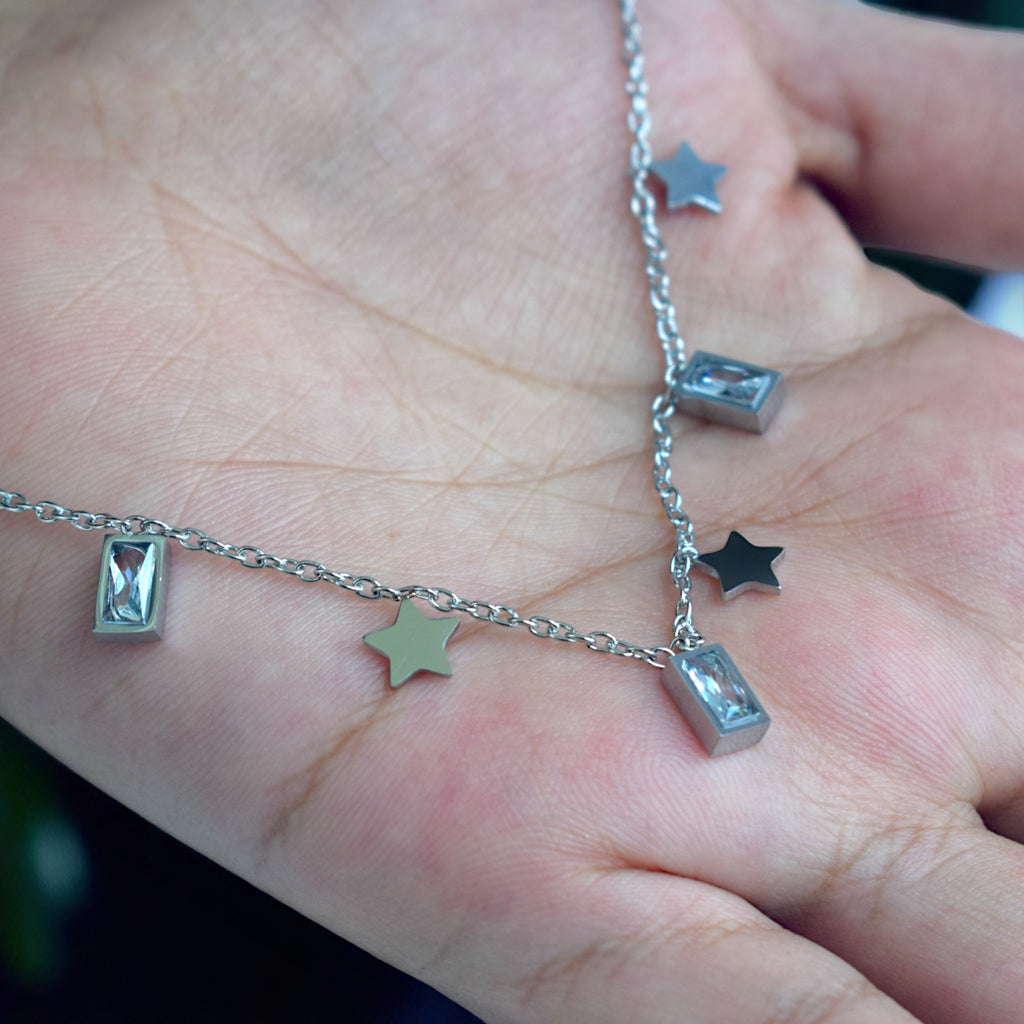 Silver necklace with star and hourglass pendants on a hand.