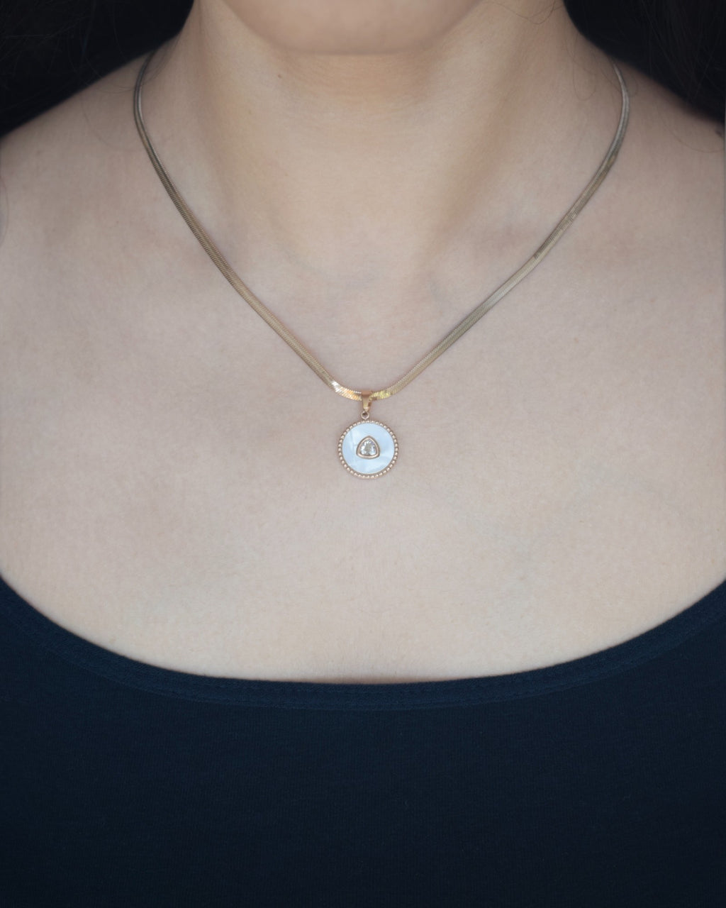 Gold necklace with a round pendant on a person wearing a black top.
