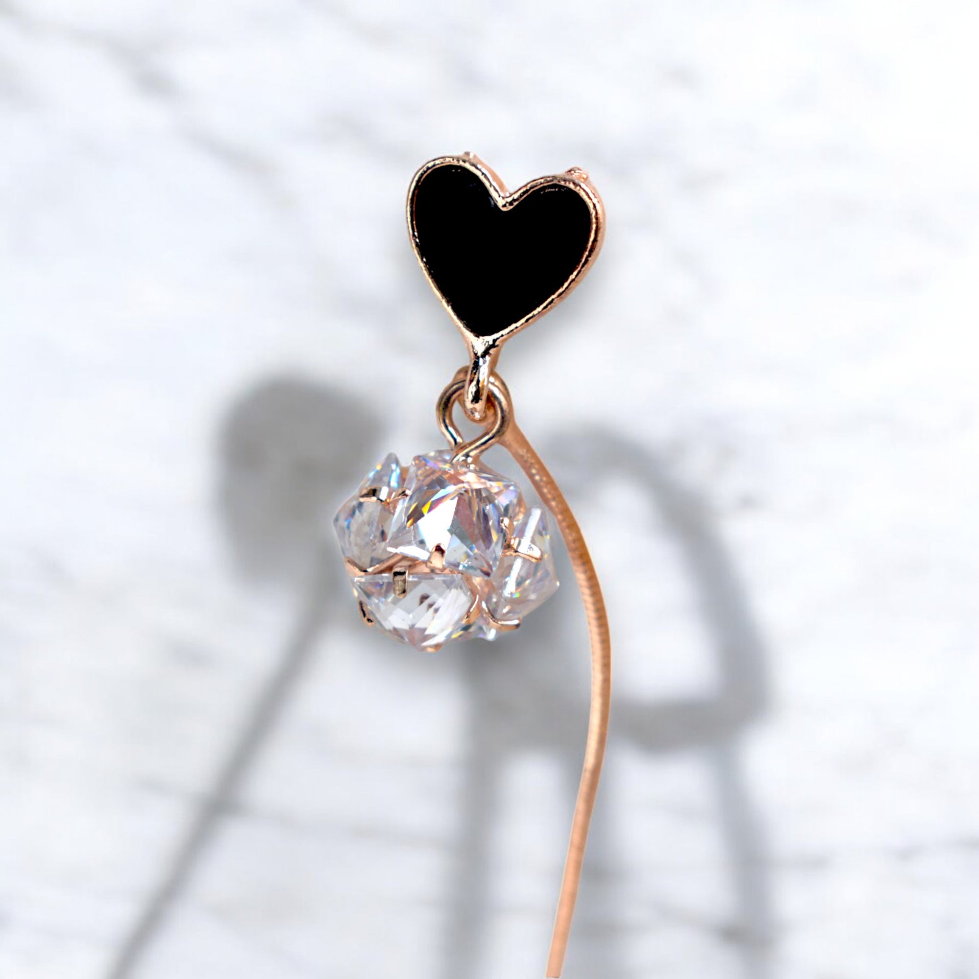 Close up of a single Rose gold heart earrings with Round zirconia diamonds on a white marble floor