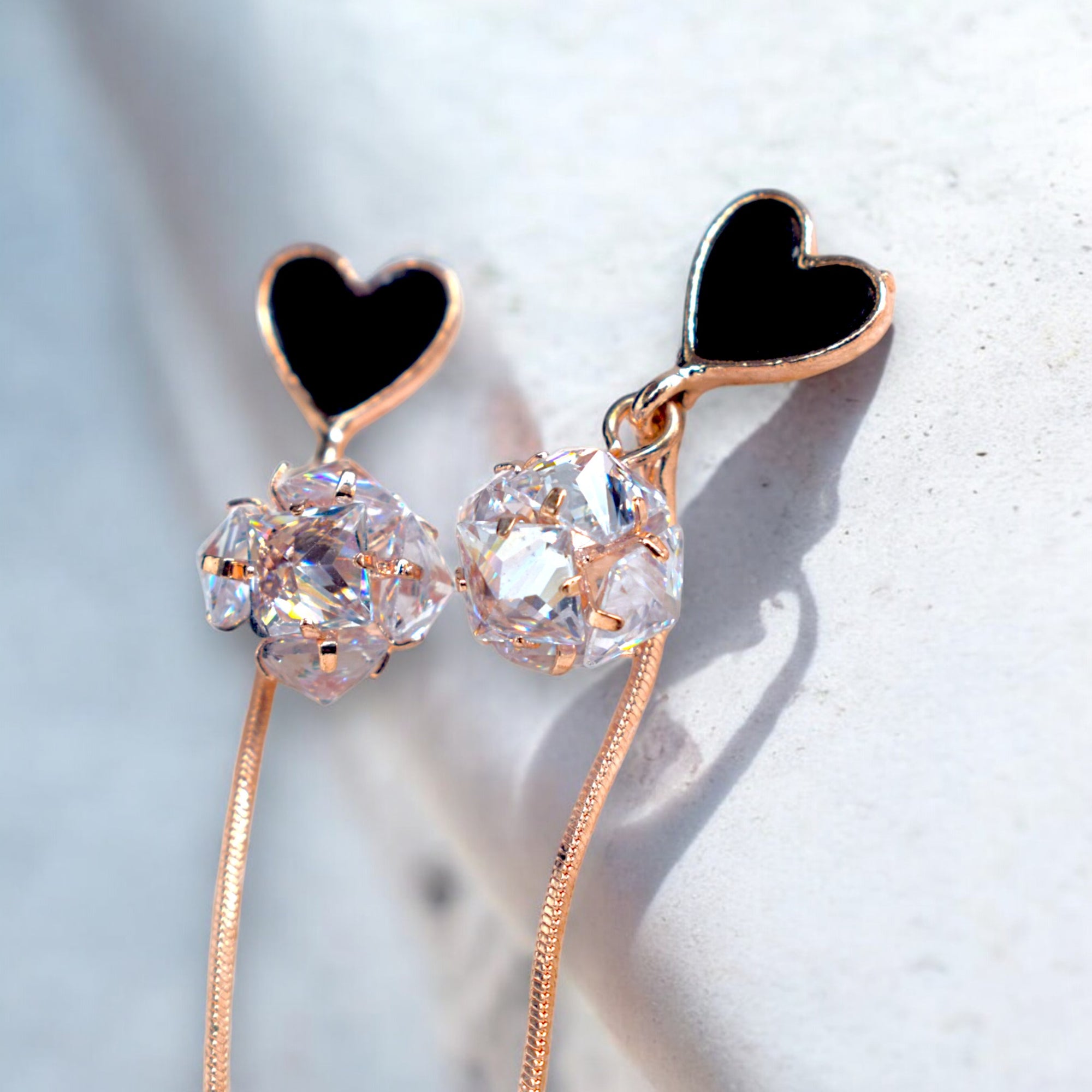 Close up of a Rose gold heart earrings with Round zirconia diamonds on a white marble floor