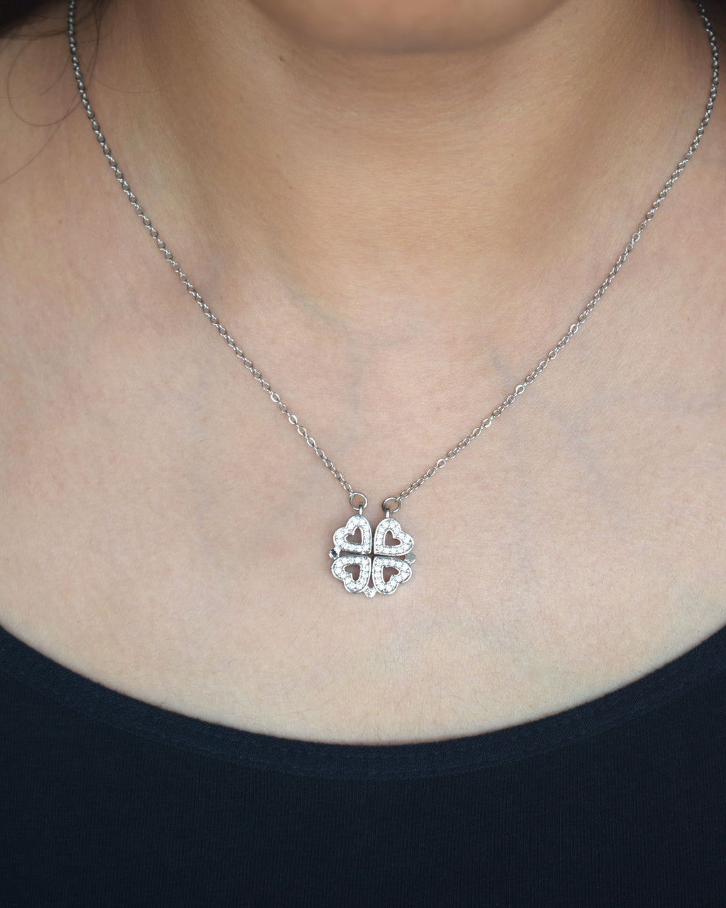 Silver necklace with a clover-shaped pendant worn by a person.