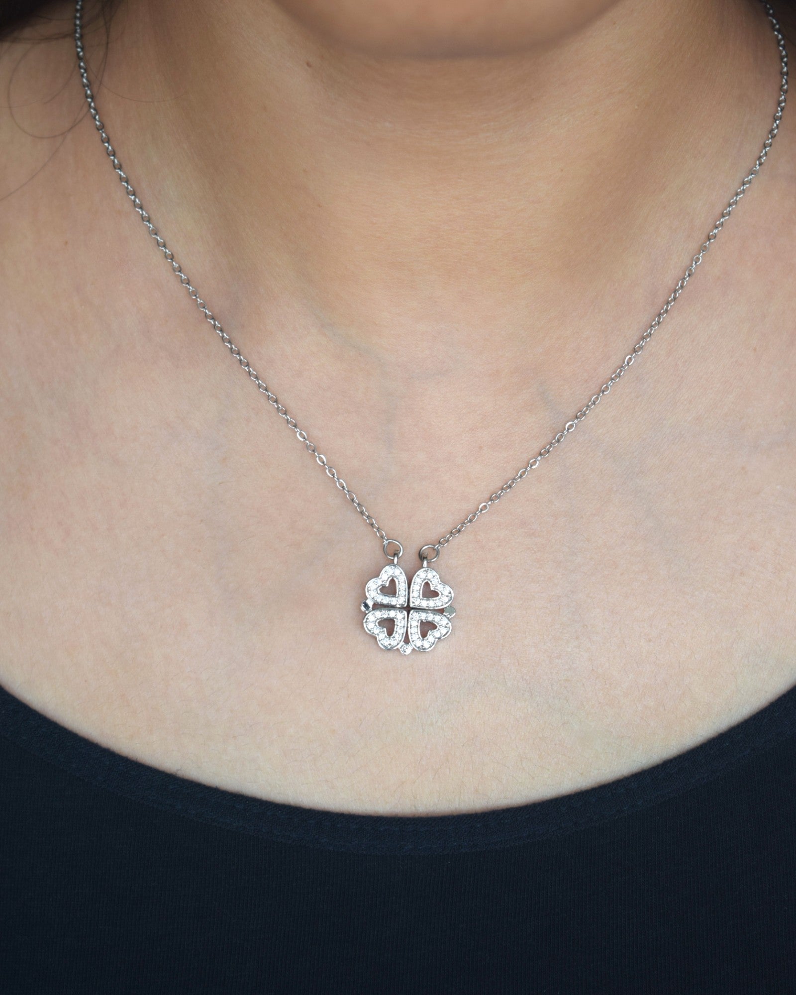 Silver necklace with a clover-shaped pendant worn by a person.